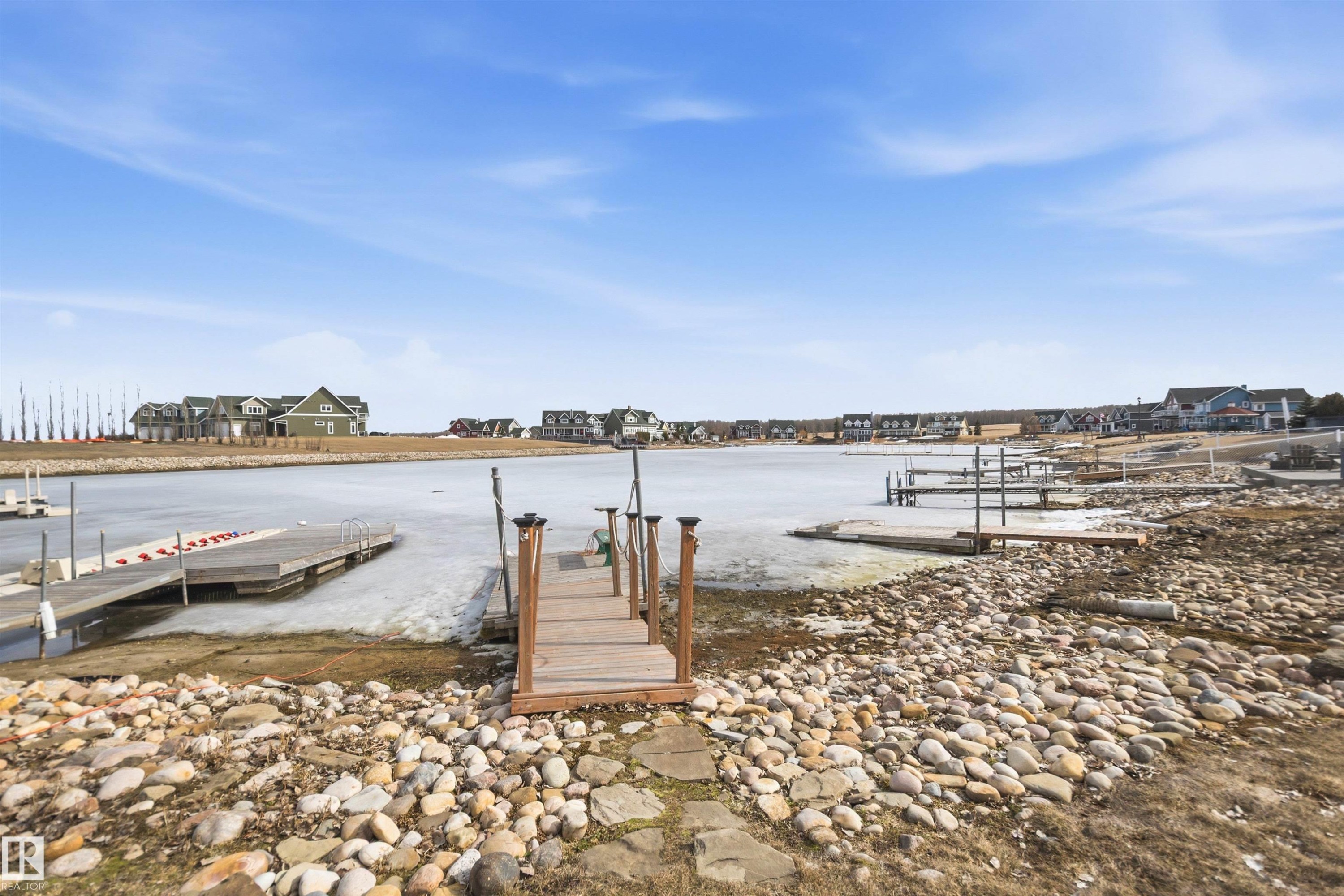 The property offers direct access to the water with a private wooden dock, set against a backdrop of a clear blue sky - 17 Sunset Harbour, Rural Wetaskiwin County, AB - Outdoor With Body Of Water With View