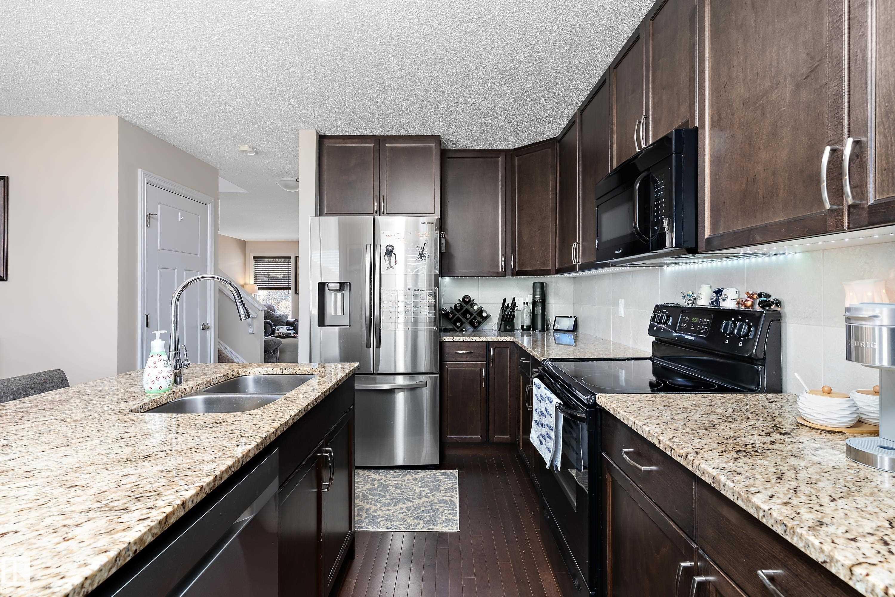 The kitchen features granite countertops, dark wood cabinetry, and stainless steel appliances, including a refrigerator and a double sink with a gooseneck faucet - 6822 Cardinal Link, Edmonton, AB - Indoor Photo Showing Kitchen With Double Sink With Upgraded Kitchen