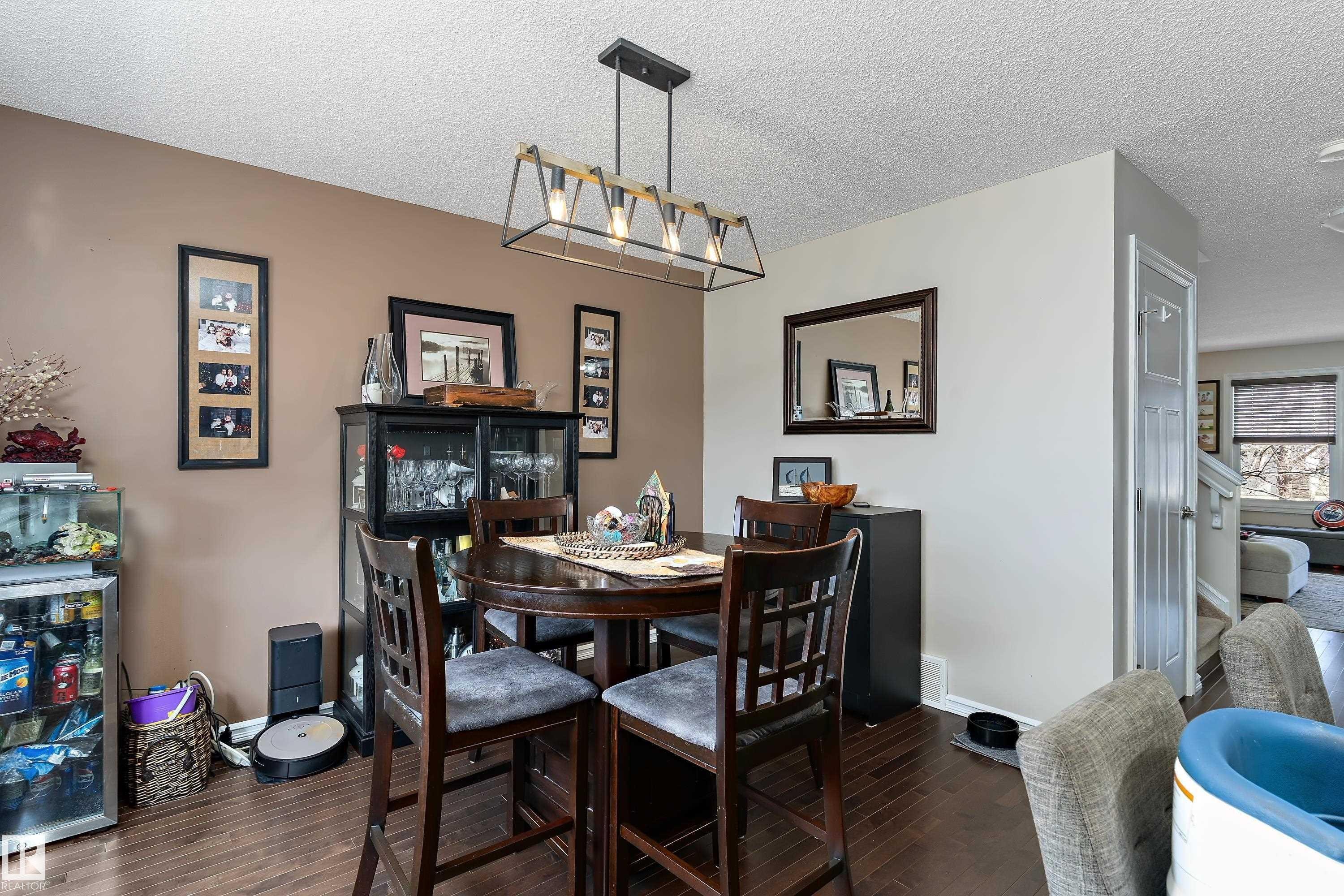 This dining area features hardwood flooring, a contemporary chandelier, and a decorative wall mirror - 6822 Cardinal Link, Edmonton, AB - Indoor Photo Showing Dining Room