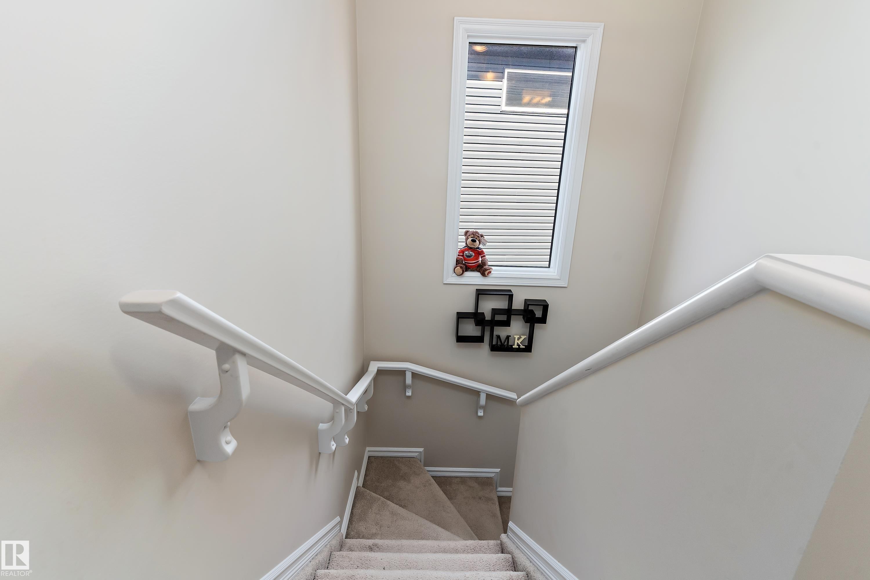 The staircase features neutral-toned carpeted steps, white wall-mounted handrails, and a window with horizontal blinds - 6822 Cardinal Link, Edmonton, AB - Indoor Photo Showing Other Room