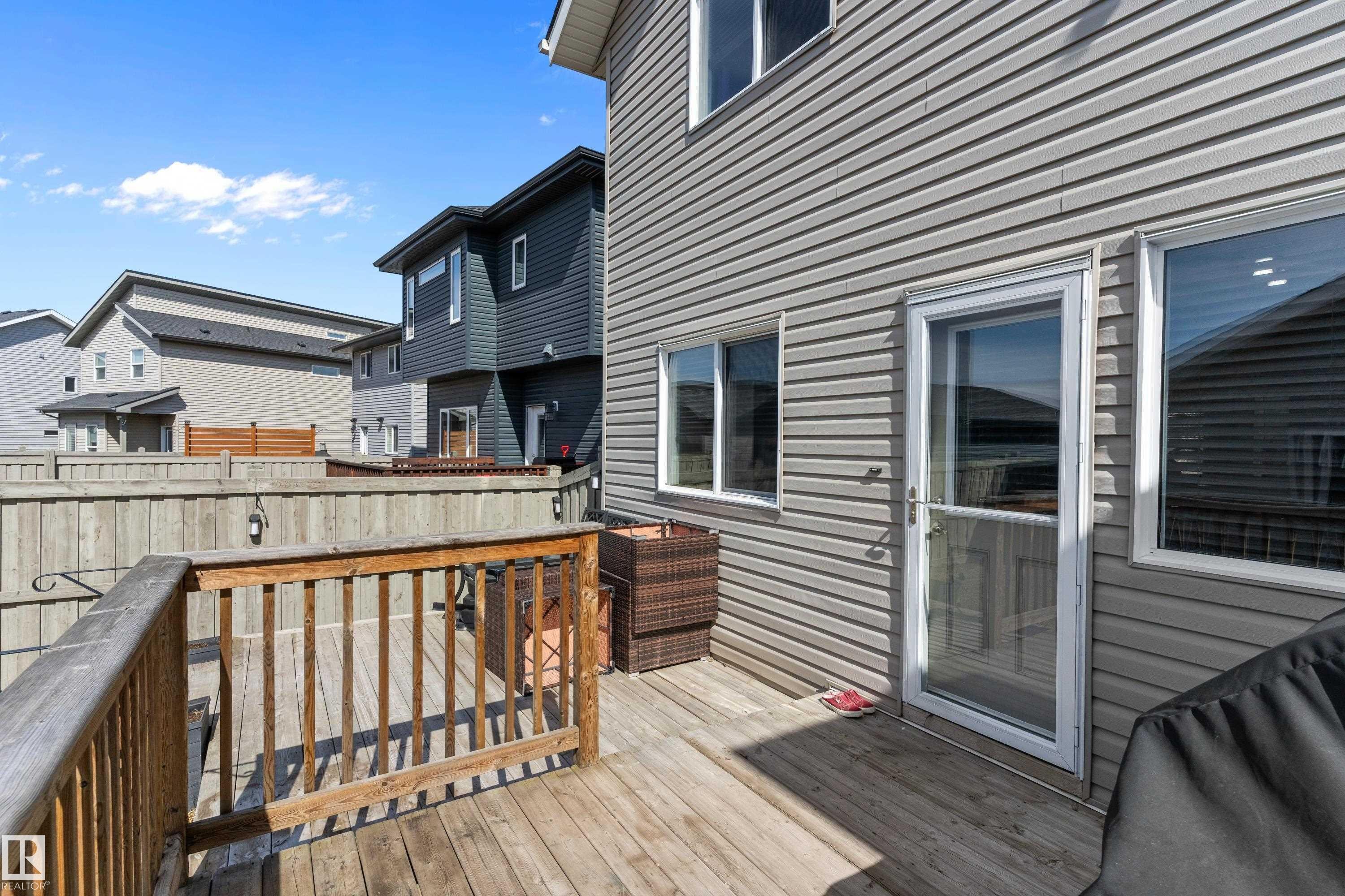 The property features an exterior with gray siding, multiple windows, and a glass-paneled door, opening onto a wooden deck with a wooden railing - 6822 Cardinal Link, Edmonton, AB - Outdoor With Deck Patio Veranda With Exterior