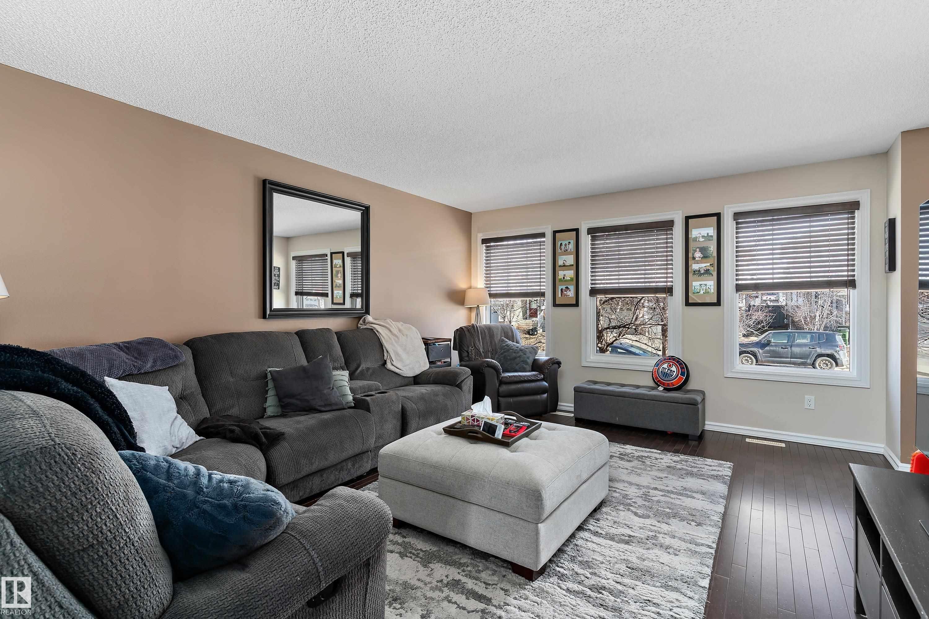 Living room featuring rich hardwood flooring, a neutral wall color, and windows with blinds that provide natural light - 6822 Cardinal Link, Edmonton, AB - Indoor Photo Showing Living Room