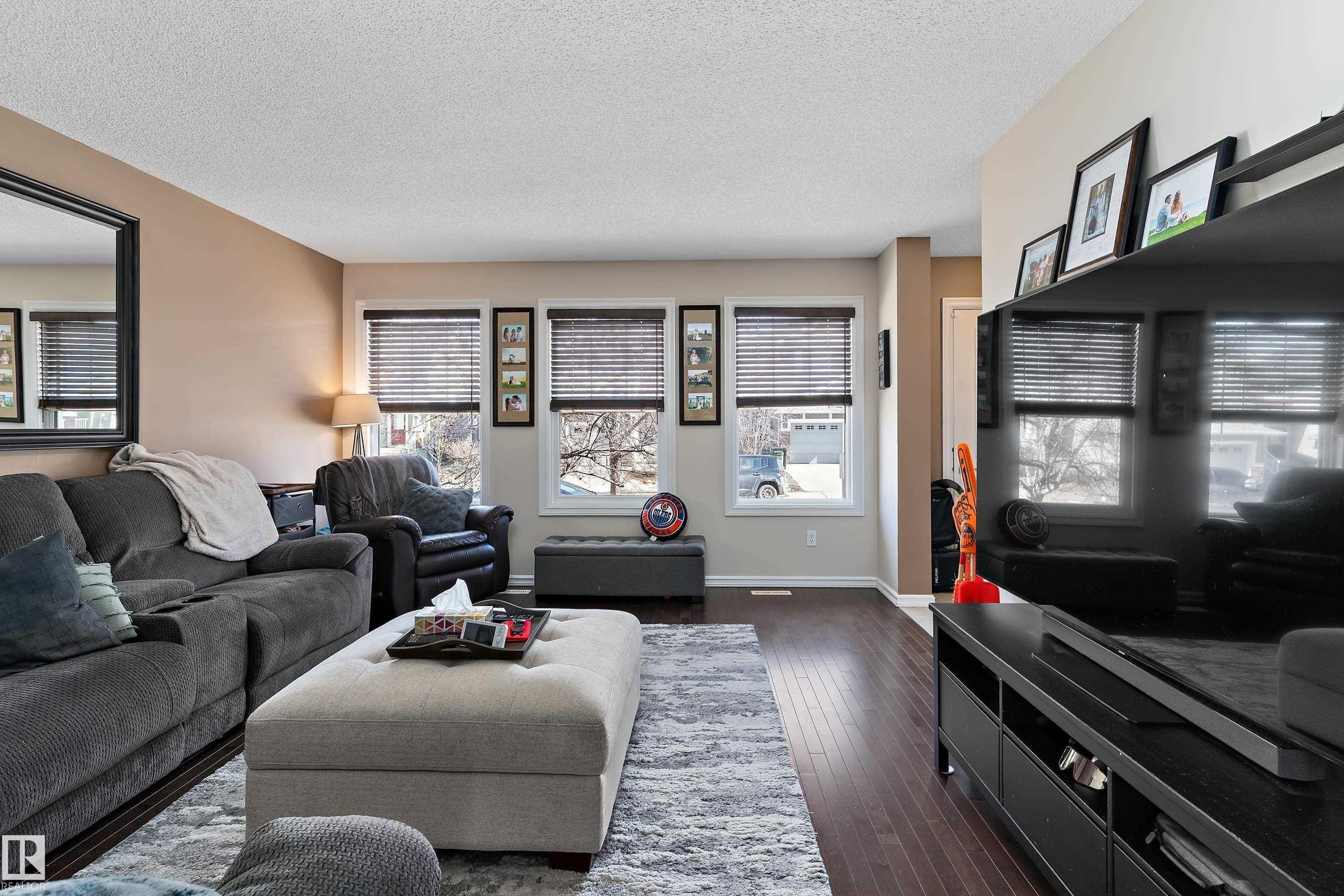 Living area featuring dark wood flooring, light-colored walls, and windows with blinds - 6822 Cardinal Link, Edmonton, AB - Indoor Photo Showing Living Room