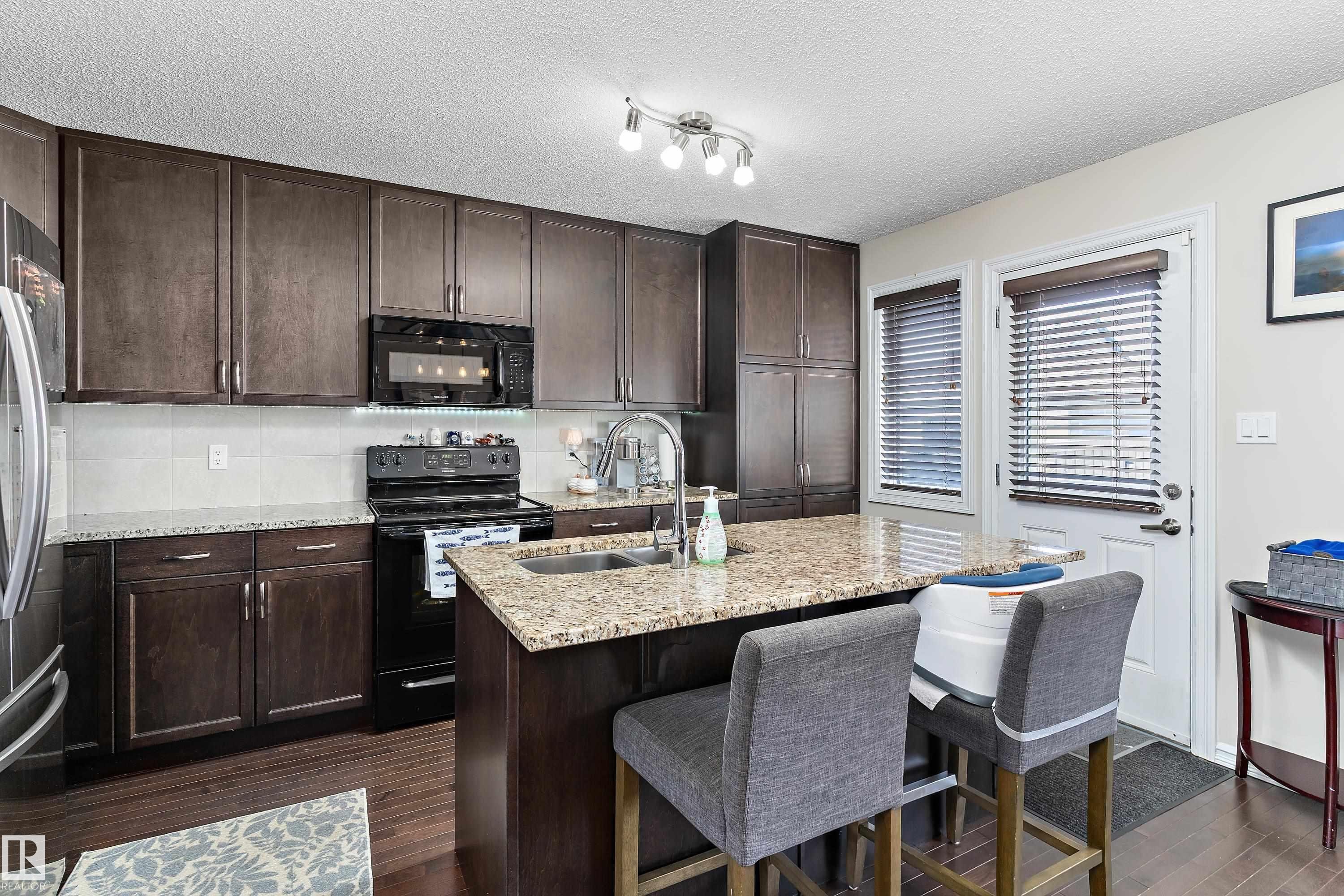 Well-appointed kitchen featuring dark wood cabinetry, granite countertops, and stainless steel appliances - 6822 Cardinal Link, Edmonton, AB - Indoor Photo Showing Kitchen With Double Sink