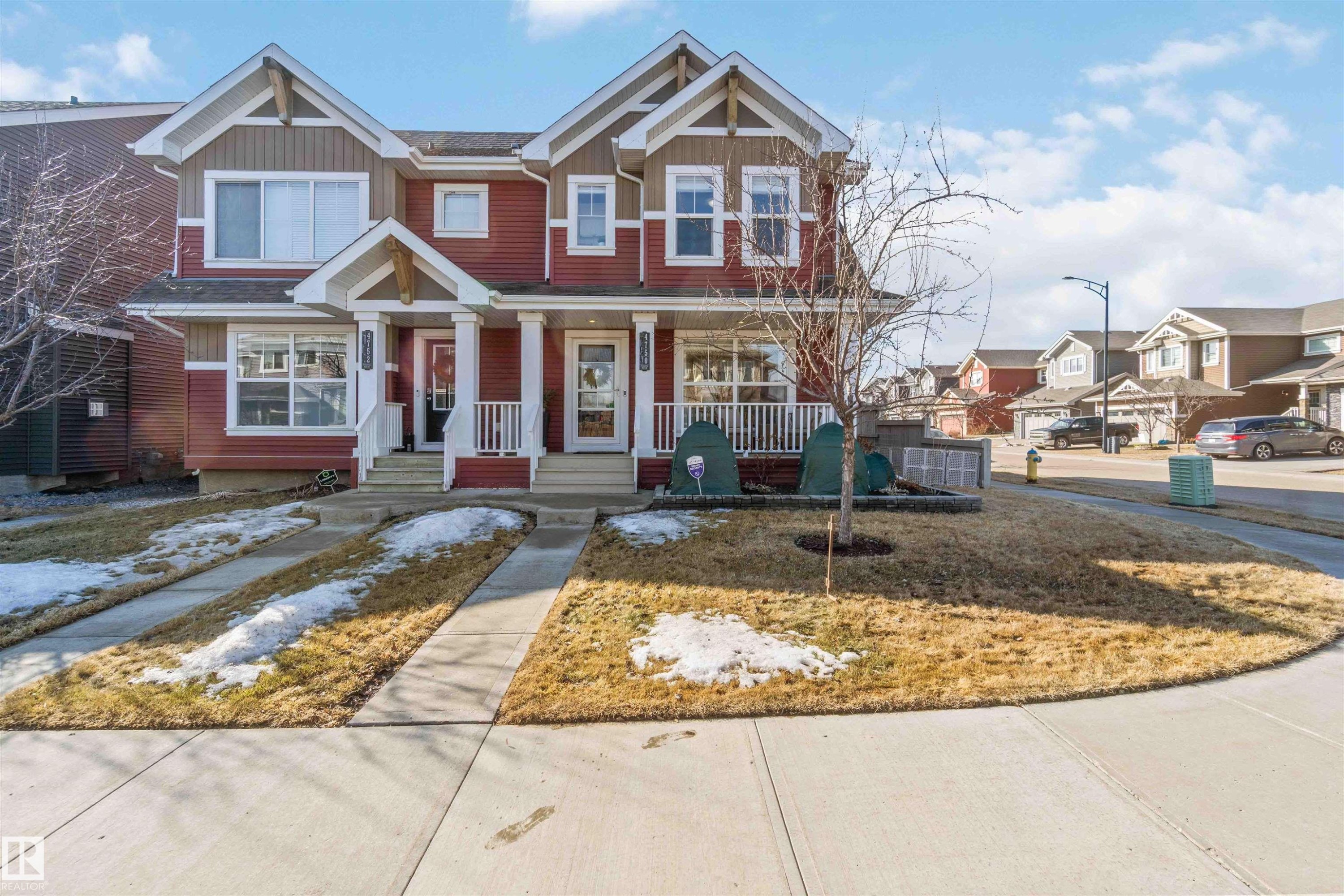 The property features a red and brown exterior with white trim, a covered front porch with white railings, and a paved walkway leading to the entrance - 4750 Crabapple Run, Edmonton, AB - Outdoor With Facade