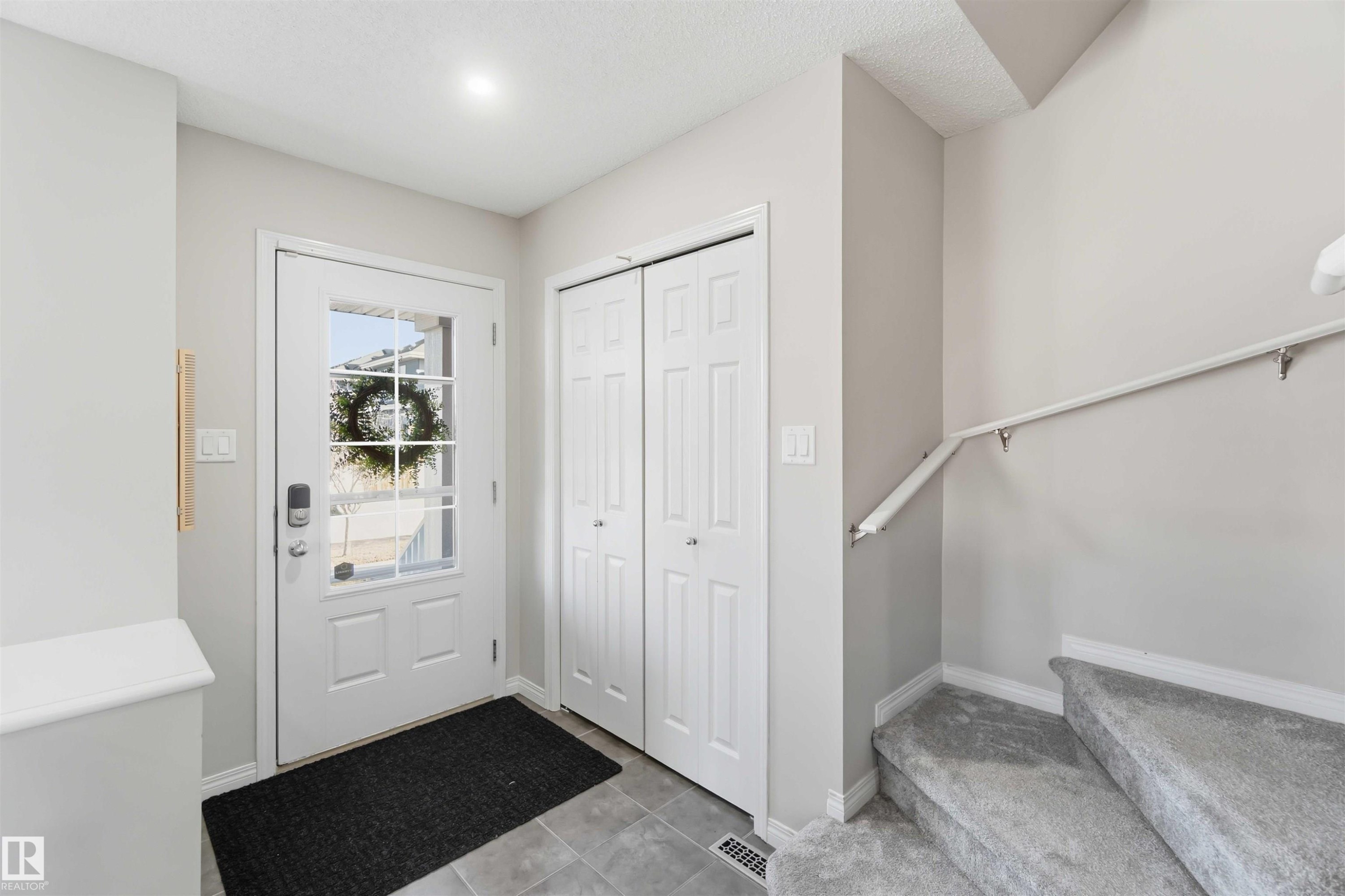 Inviting entry foyer featuring a white paneled door with windowpanes, a closet with bi-fold doors, and a carpeted staircase with a handrail - 4750 Crabapple Run, Edmonton, AB - Indoor Photo Showing Other Room