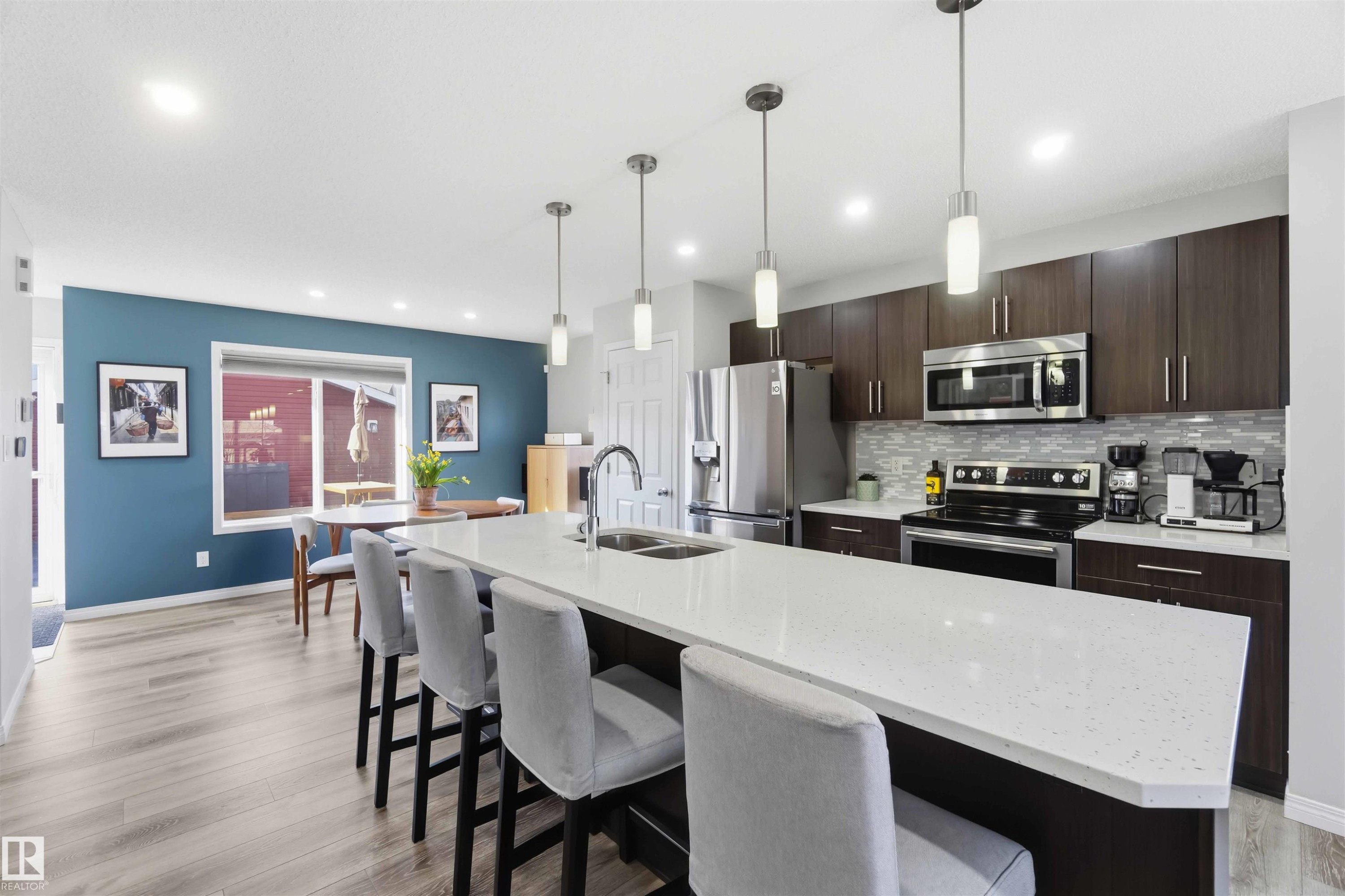 The property features an open-concept kitchen and dining area with light wood flooring, a large island with seating, dark wood cabinetry, and stainless steel appliances - 4750 Crabapple Run, Edmonton, AB - Indoor Photo Showing Kitchen With Stainless Steel Kitchen With Double Sink With Upgraded Kitchen