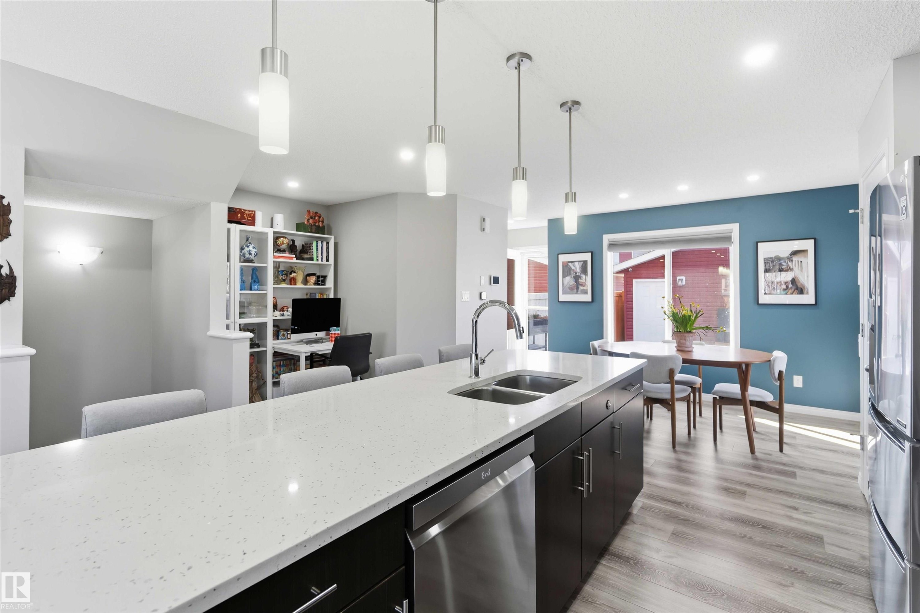 Kitchen featuring a large island with a light-colored countertop and double sink, dark cabinetry, and stainless steel appliances - 4750 Crabapple Run, Edmonton, AB - Indoor Photo Showing Kitchen With Stainless Steel Kitchen With Double Sink With Upgraded Kitchen