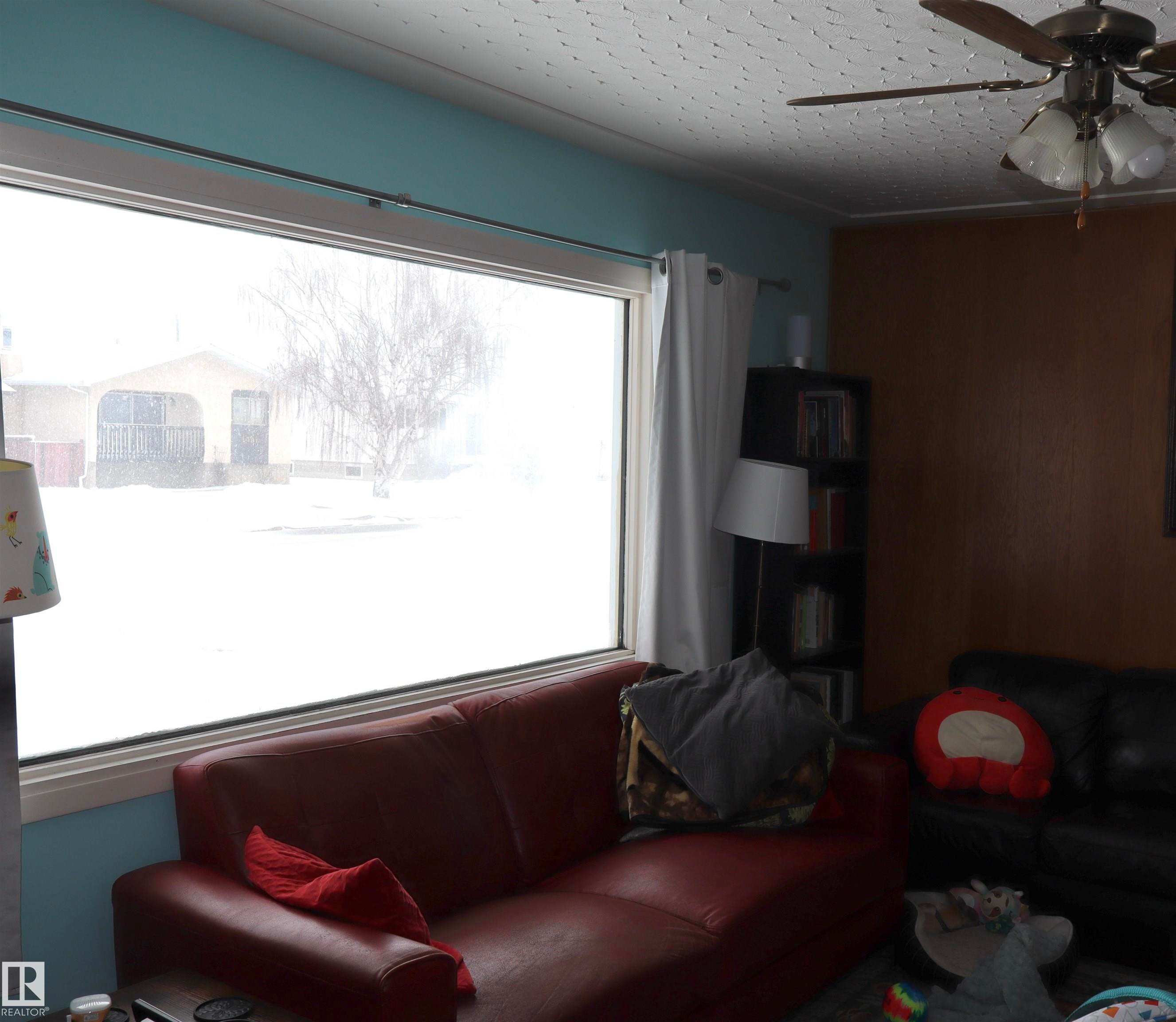 Living area featuring a large window, a ceiling fan with light fixture, and a bookcase - 4315 56 Avenue, Barrhead, AB - Indoor