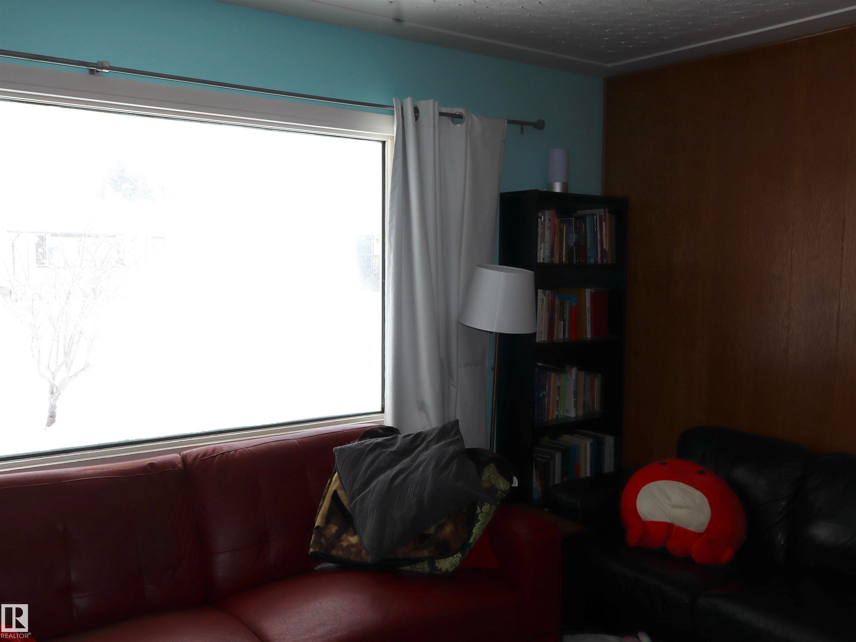 Living space featuring a large window, a partial accent wall, and a light blue wall - 4315 56 Avenue, Barrhead, AB - Indoor