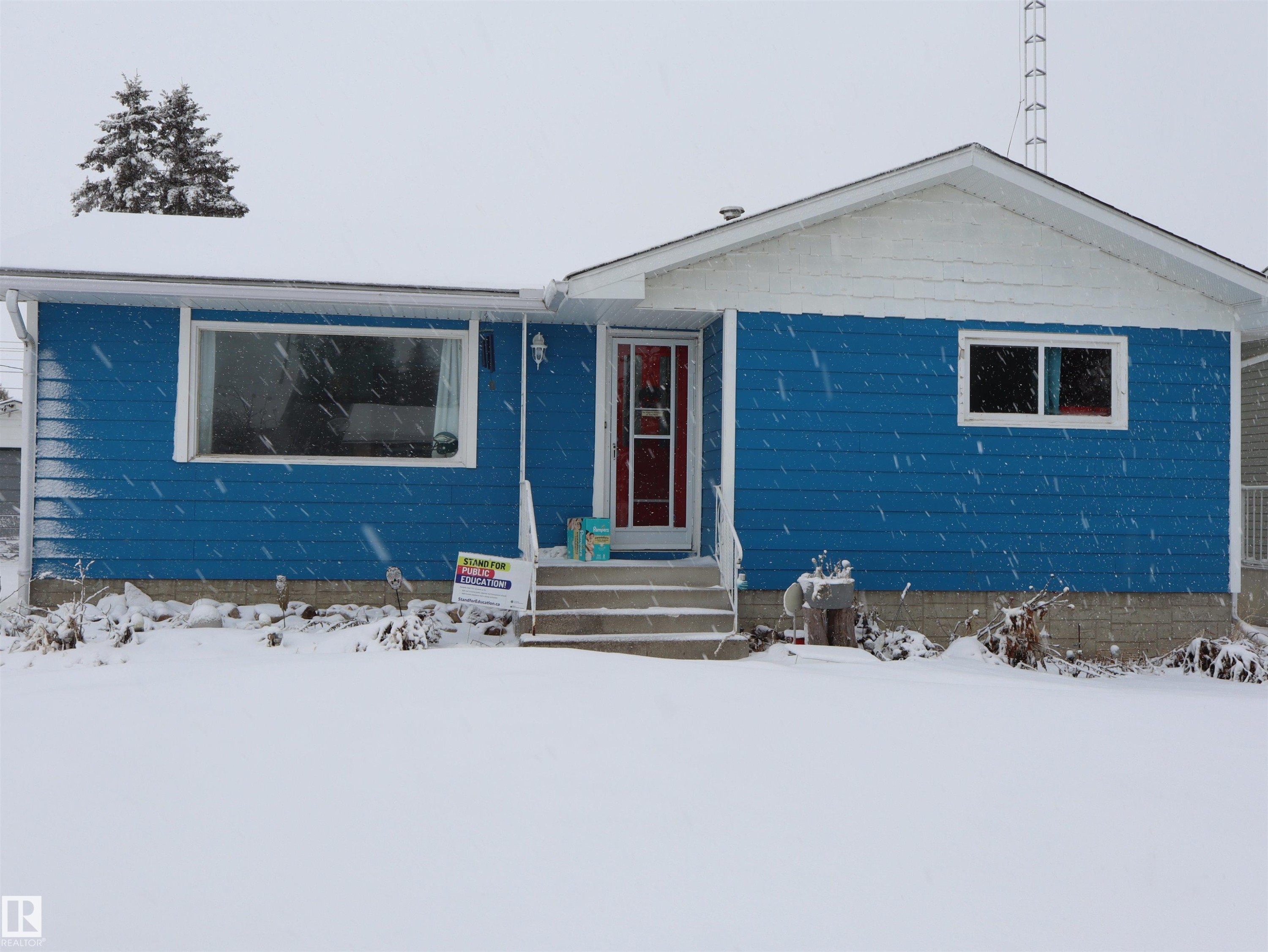 The property features blue siding with white trim, a red entrance door, and a front yard - 4315 56 Avenue, Barrhead, AB - Outdoor