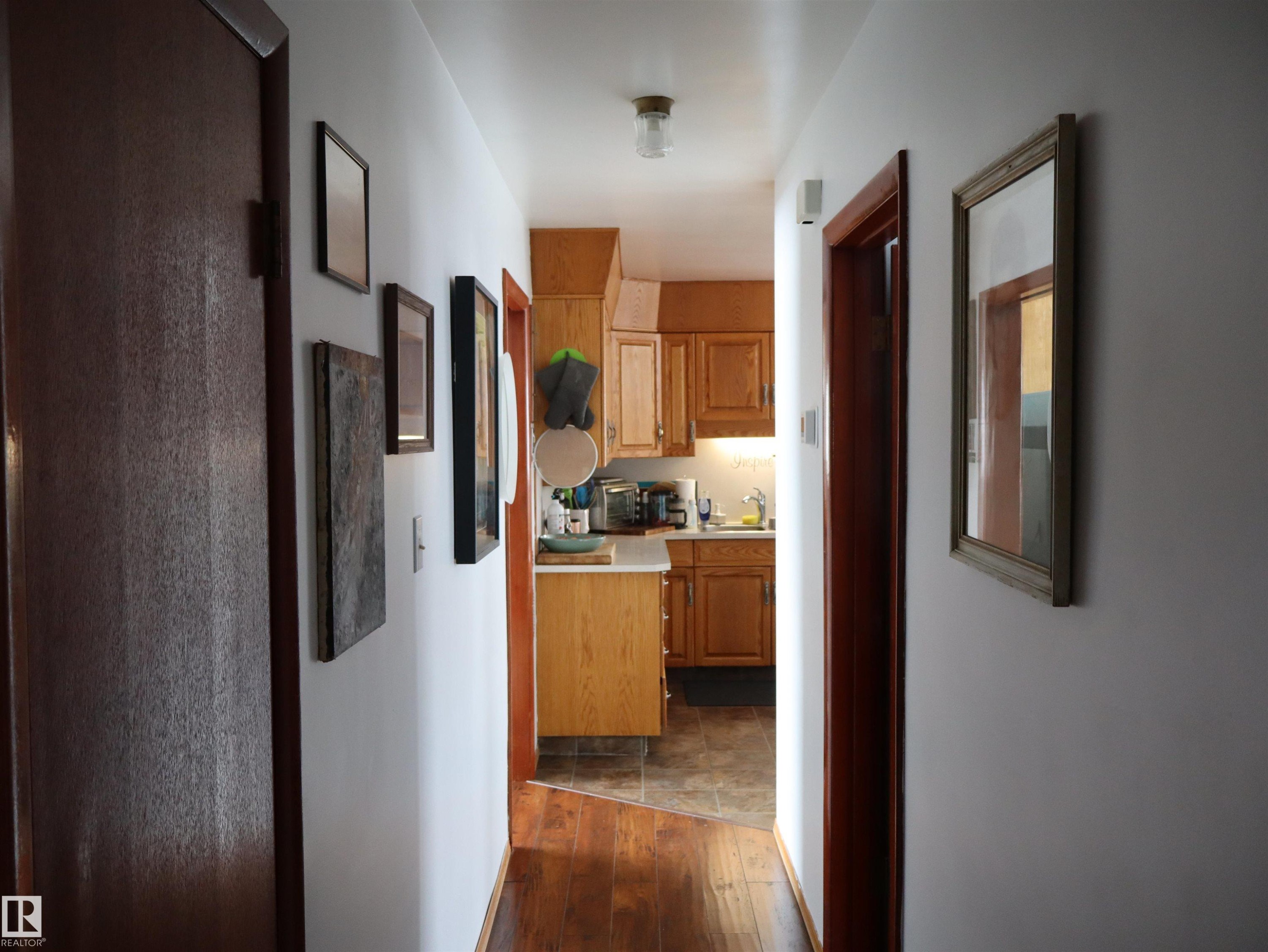Hallway with hardwood flooring leading to a kitchen with wood cabinetry, a tiled floor, and a ceiling-mounted light fixture - 4315 56 Avenue, Barrhead, AB - Indoor Photo Showing Other Room