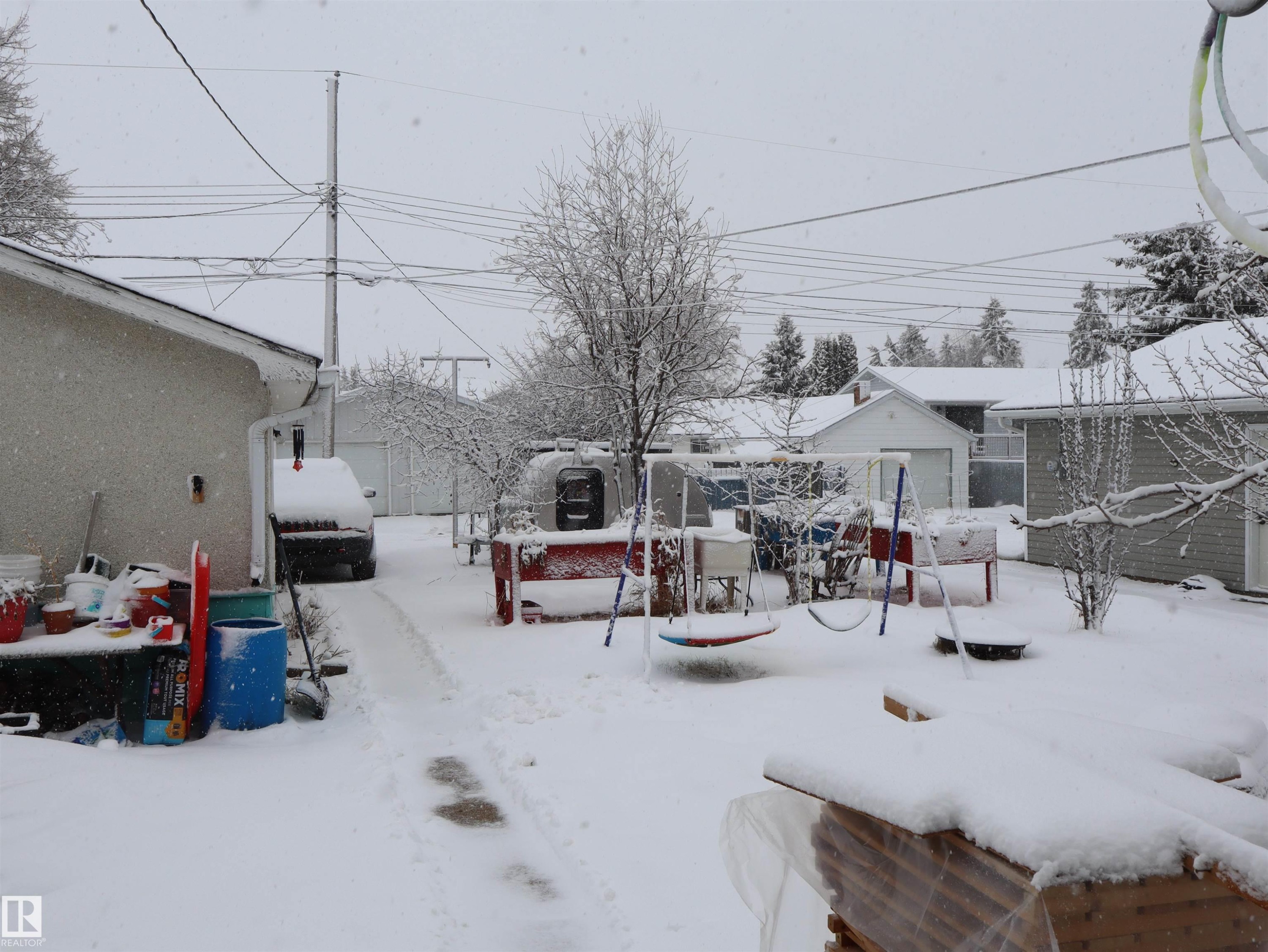 The property features a spacious backyard with a snow-covered lawn and mature trees - 4315 56 Avenue, Barrhead, AB - Outdoor