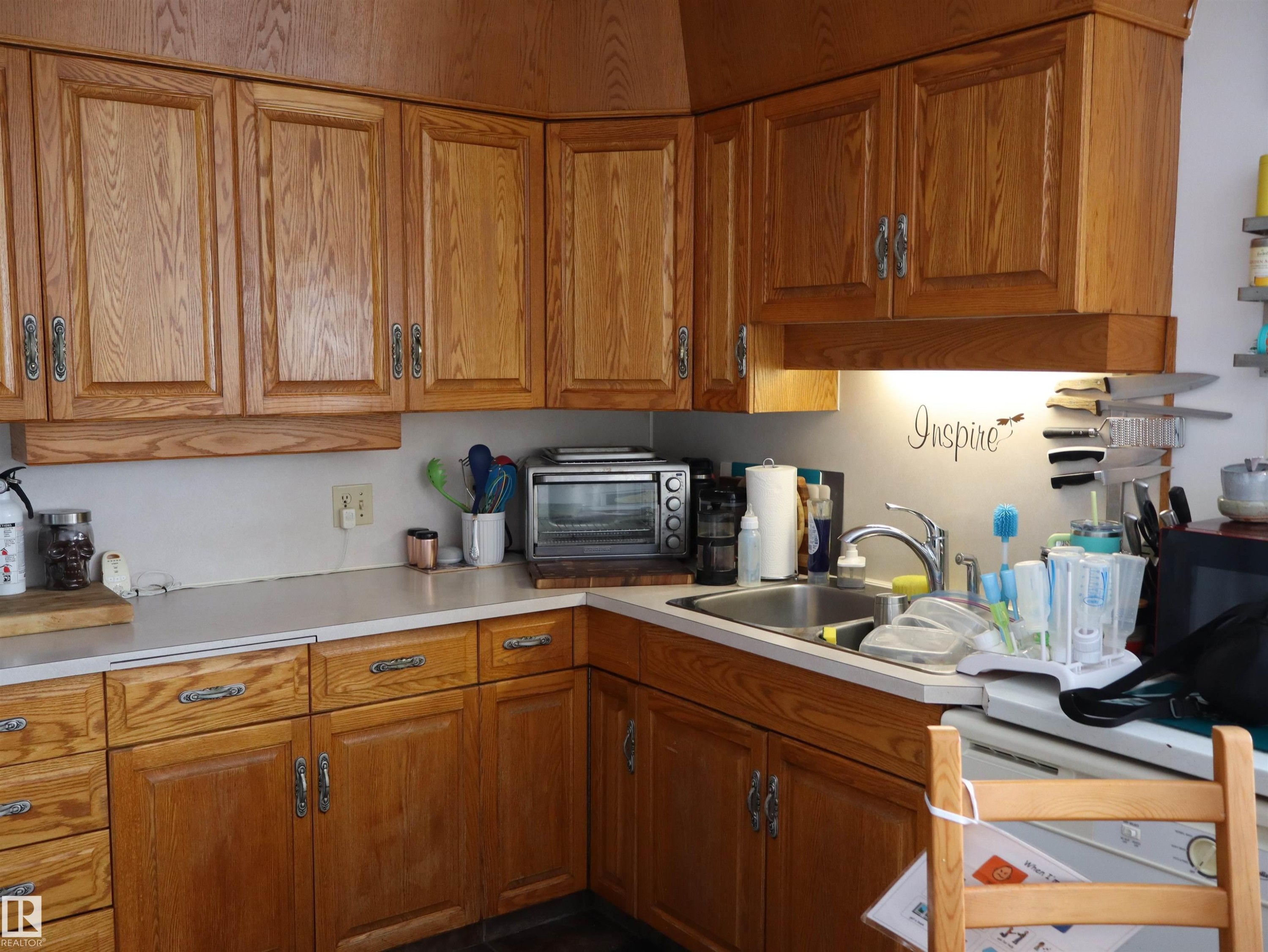 Kitchen featuring wood cabinetry with decorative hardware, white countertops, and a stainless steel sink with a chrome faucet - 4315 56 Avenue, Barrhead, AB - Indoor Photo Showing Kitchen With Double Sink