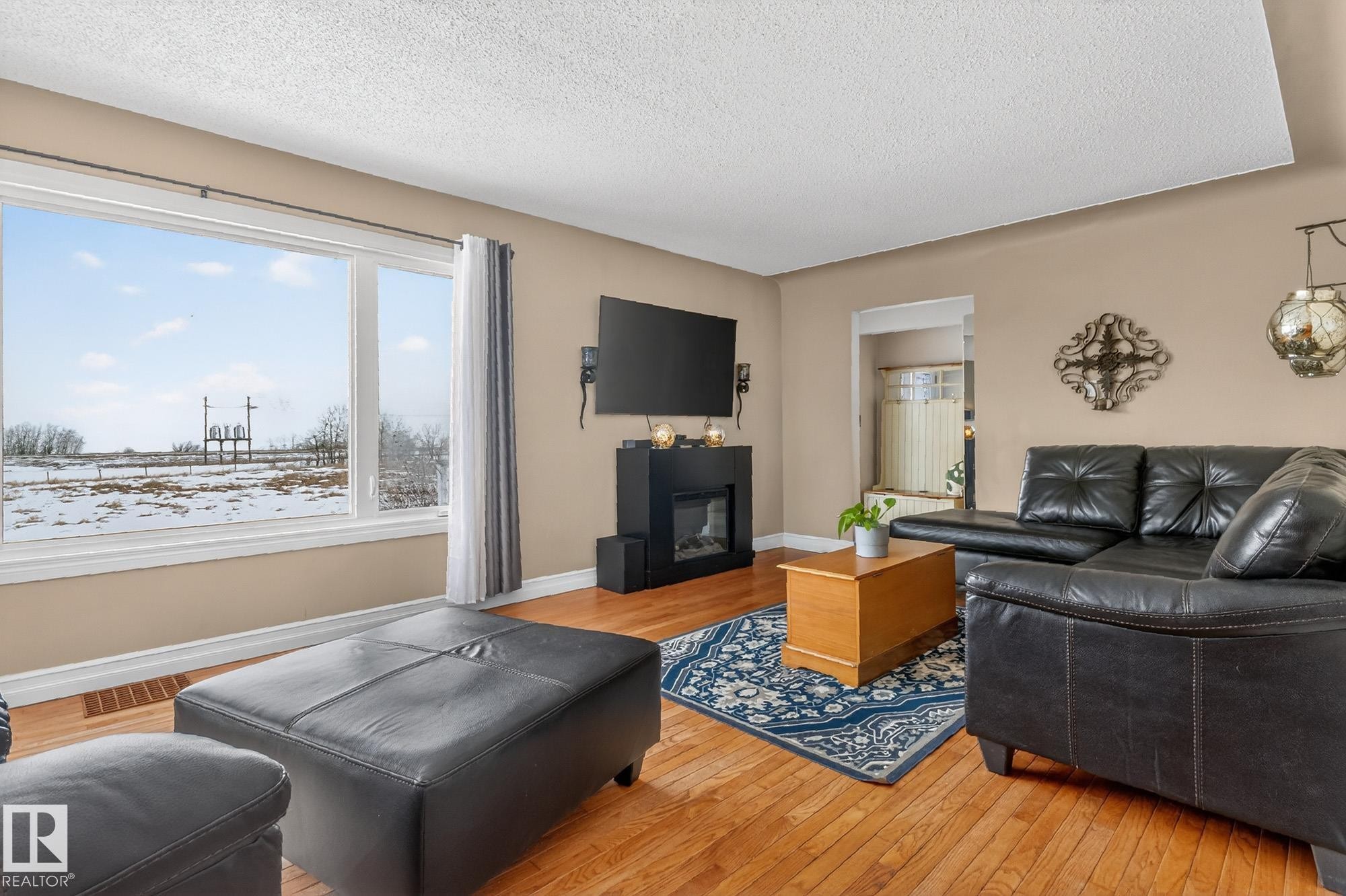 Living area featuring hardwood floors, a large window providing ample natural light, and a decorative fireplace - 160068 Twp 531, Rural Lamont County, AB - Indoor Photo Showing Living Room With Fireplace