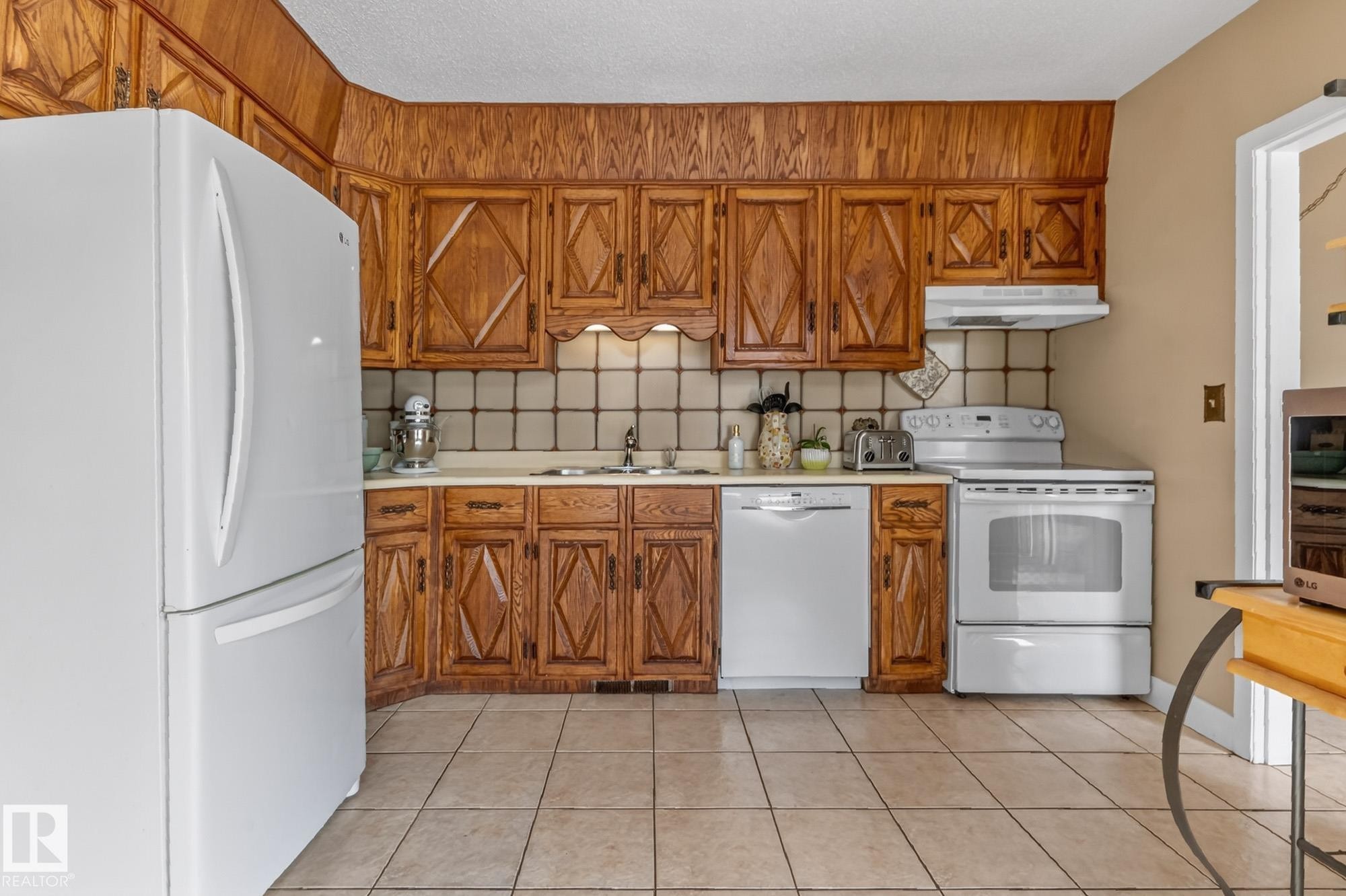 The kitchen features wood cabinetry, a tiled backsplash, and light-colored flooring - 160068 Twp 531, Rural Lamont County, AB - Indoor Photo Showing Kitchen