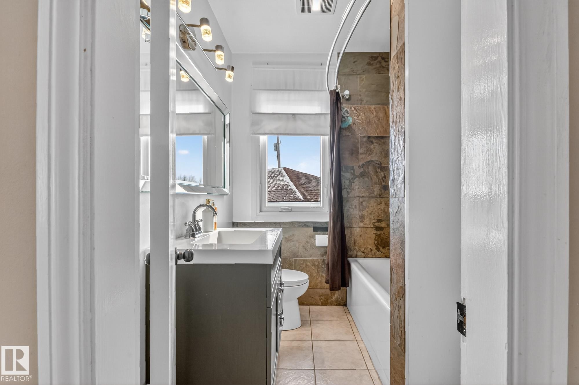 The bathroom features a vanity with a sink, a mirror with overhead lighting, and a bathtub with a tiled surround - 160068 Twp 531, Rural Lamont County, AB - Indoor Photo Showing Bathroom