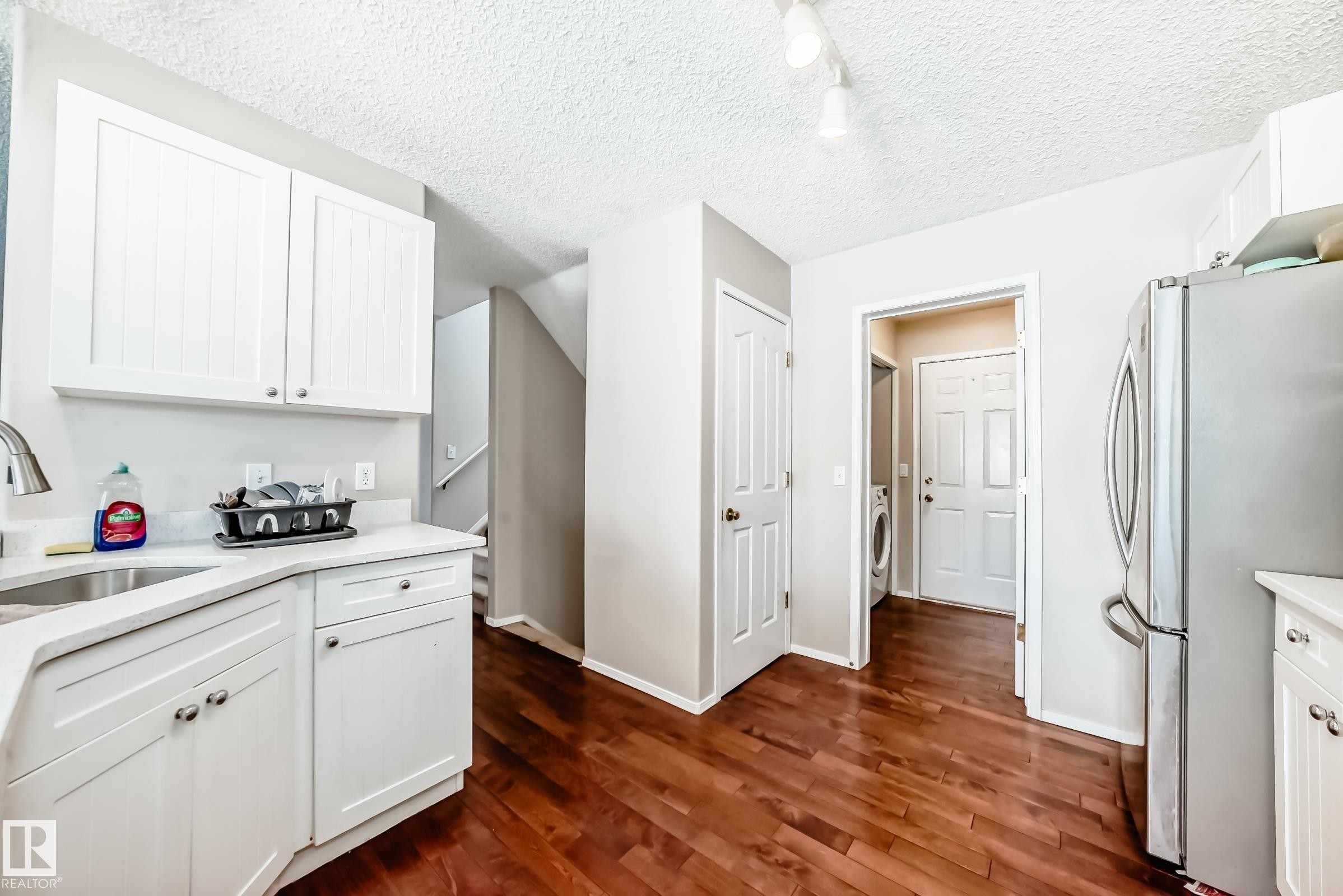 The kitchen features white cabinetry, a stainless steel refrigerator, and hardwood flooring - 19024 50 Avenue, Edmonton, AB - Indoor Photo Showing Kitchen