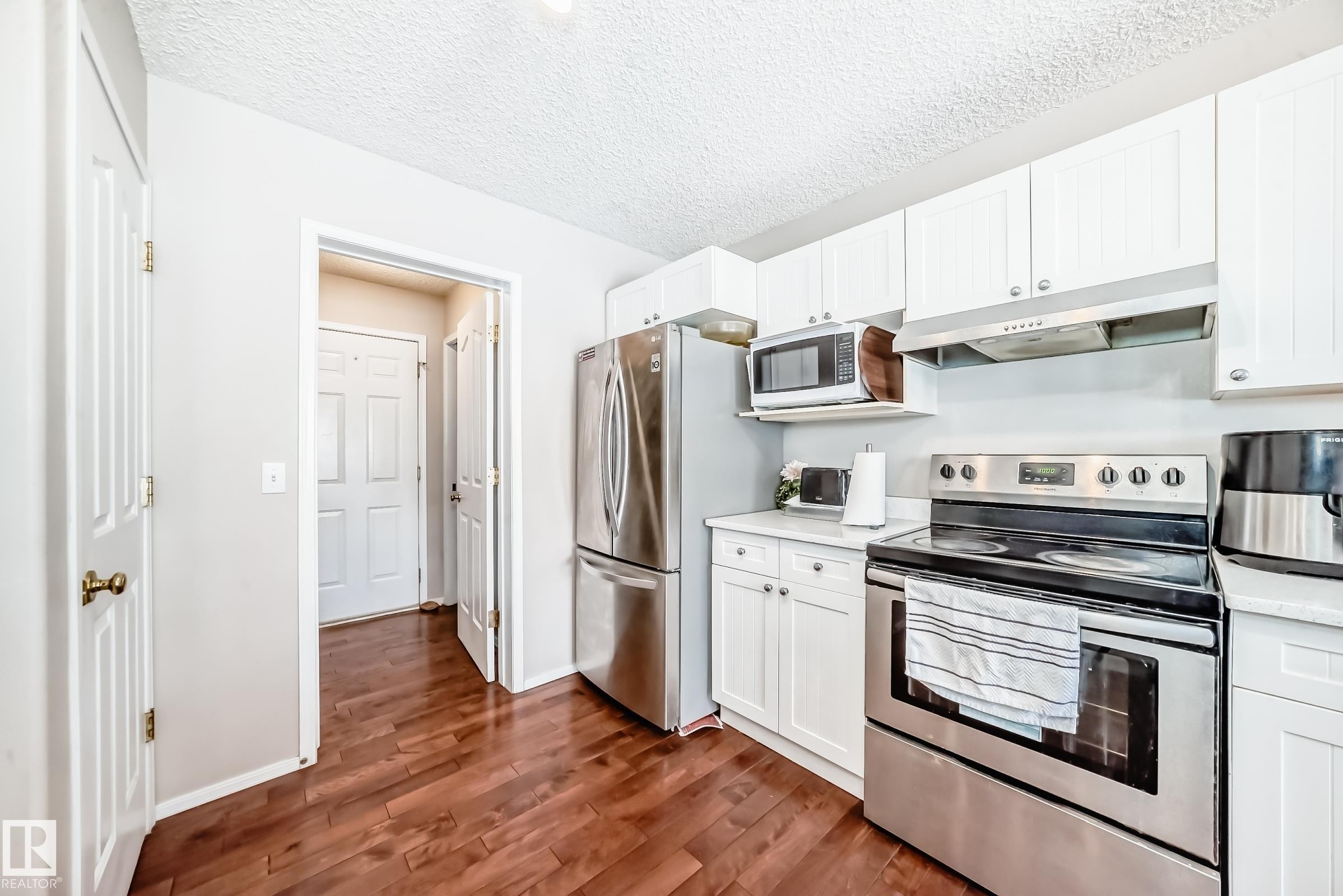 Kitchen featuring wood flooring, white cabinetry, a stainless steel refrigerator, a stainless steel range, and a stainless steel microwave - 19024 50 Avenue, Edmonton, AB - Indoor Photo Showing Kitchen