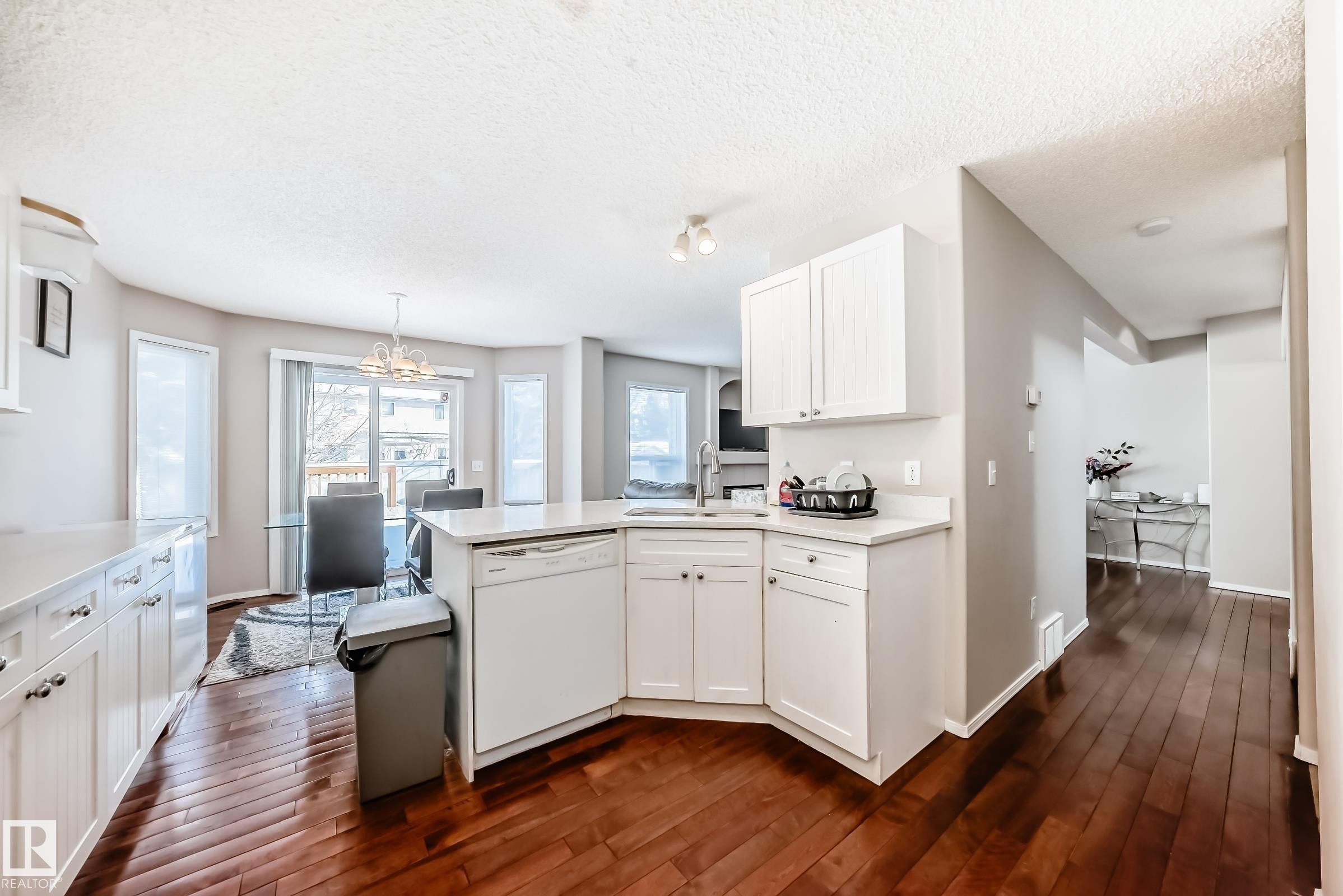 This kitchen features white cabinetry with silver hardware, a corner sink, and hardwood flooring - 19024 50 Avenue, Edmonton, AB - Indoor Photo Showing Kitchen With Upgraded Kitchen