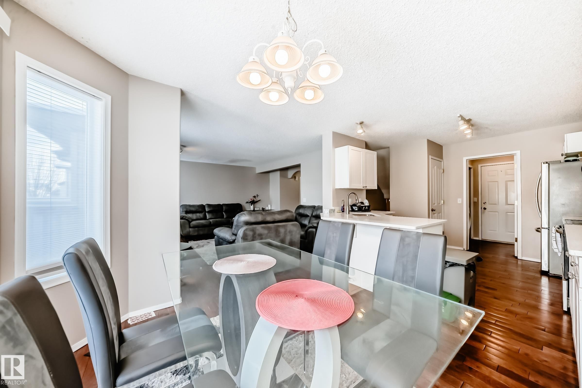 Bright dining area with a glass-top table, a white chandelier, and hardwood floors - 19024 50 Avenue, Edmonton, AB - Indoor Photo Showing Dining Room