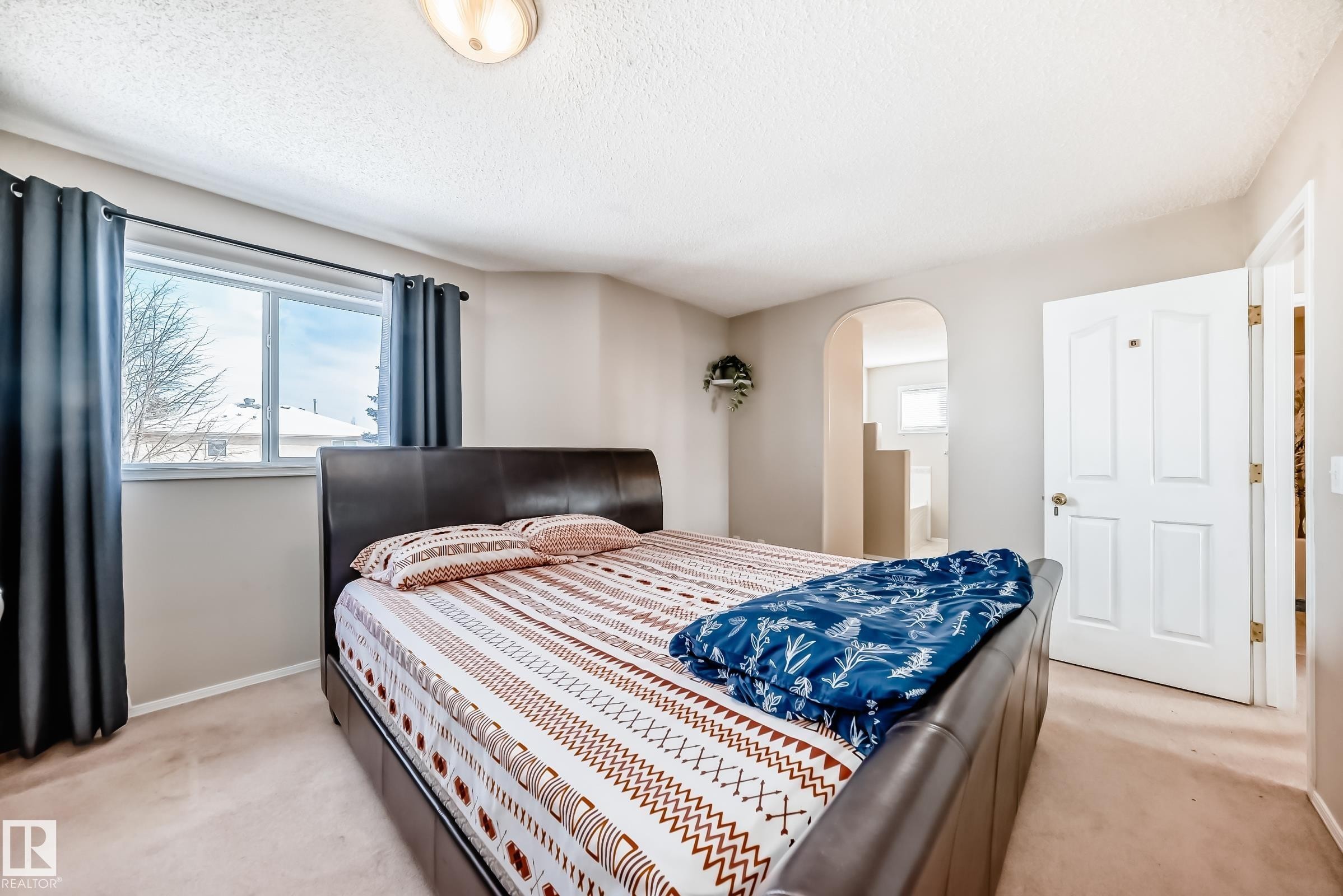 The bedroom features soft carpeting, a window with dark curtains, and an arched doorway - 19024 50 Avenue, Edmonton, AB - Indoor Photo Showing Bedroom