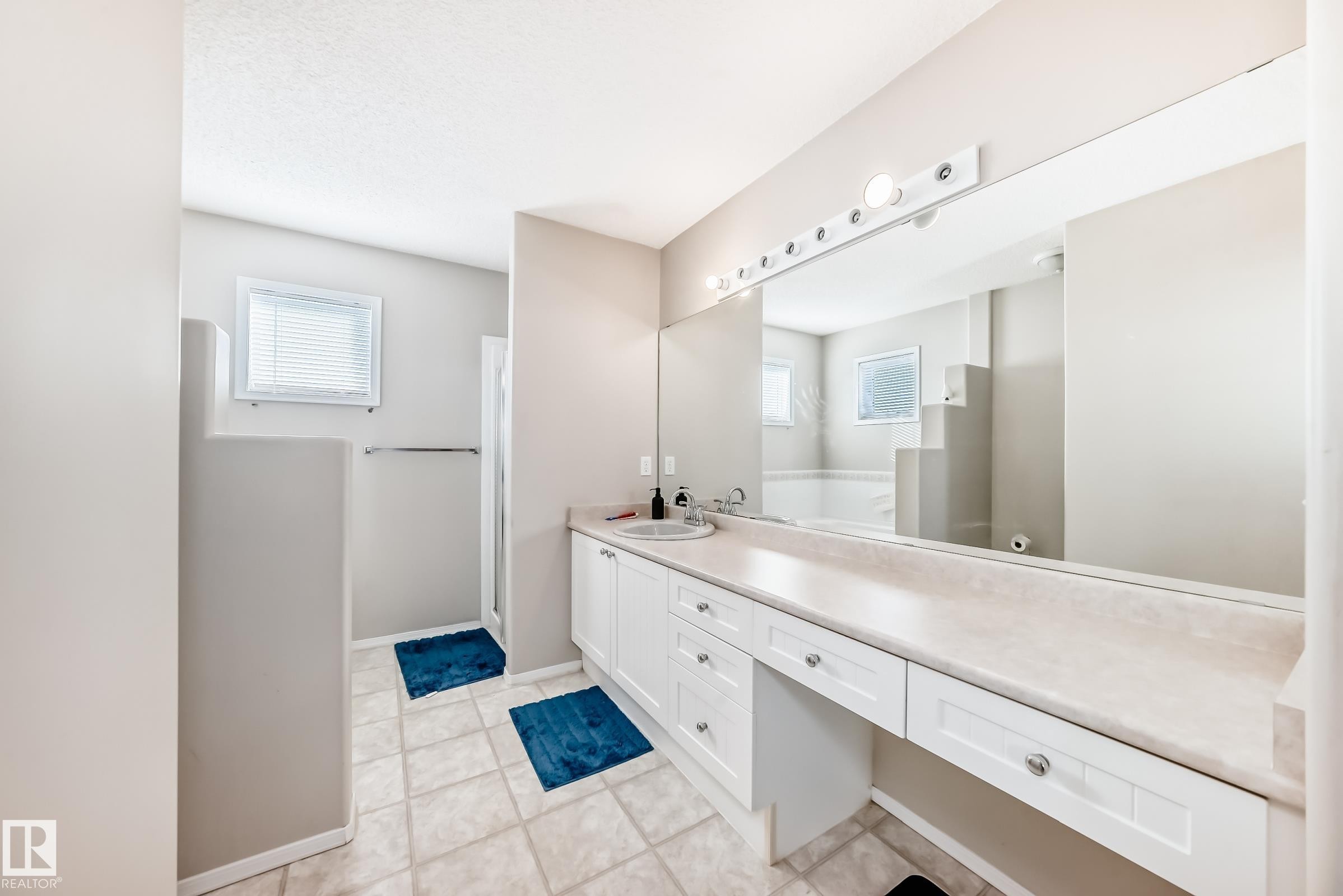 Bathroom featuring light-colored tiled flooring, a long vanity with dual sinks, and a large mirror with overhead lighting - 19024 50 Avenue, Edmonton, AB - Indoor Photo Showing Bathroom