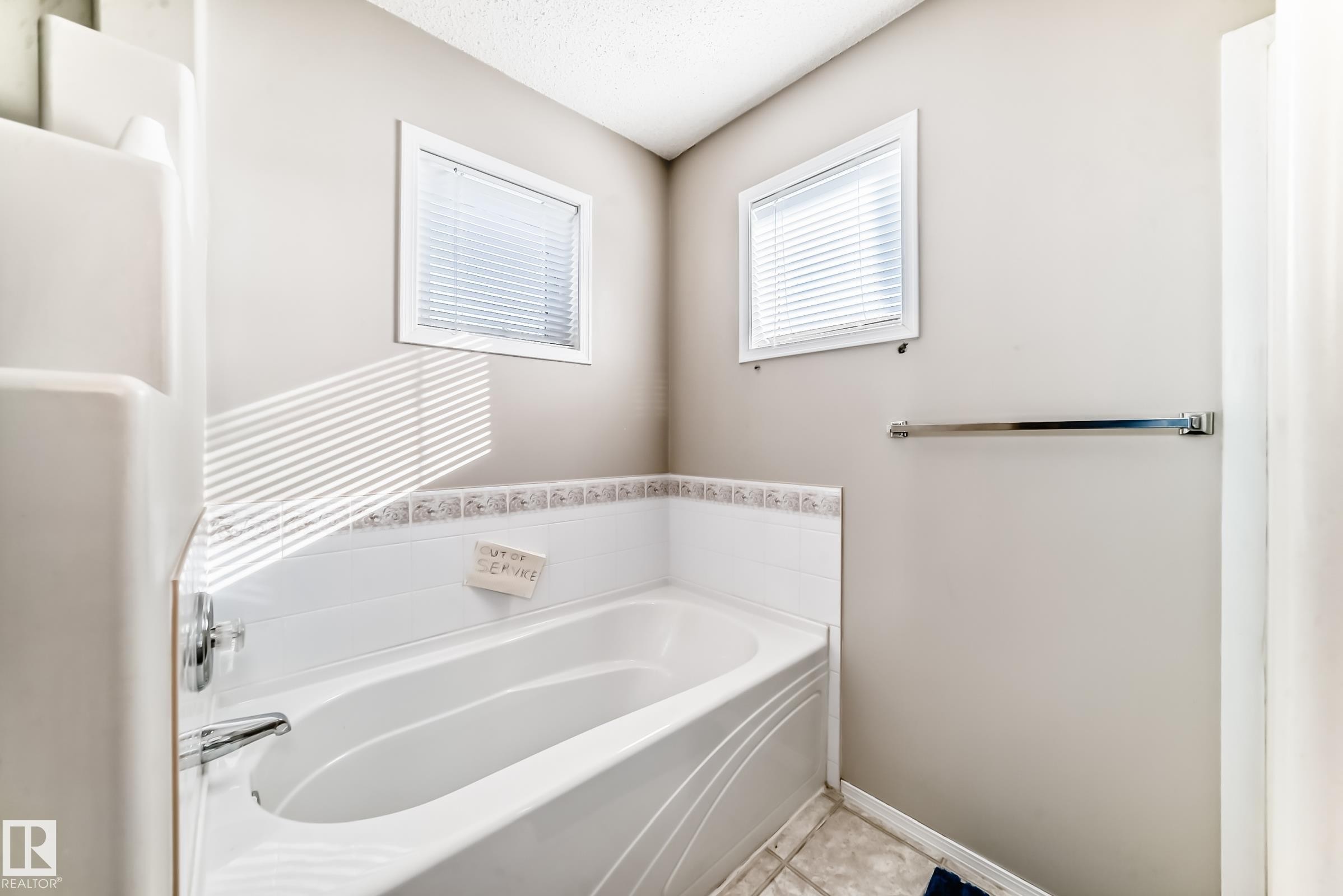 Bathroom with a built-in bathtub, two windows with blinds, and light-colored wall tiles with a decorative border - 19024 50 Avenue, Edmonton, AB - Indoor Photo Showing Bathroom