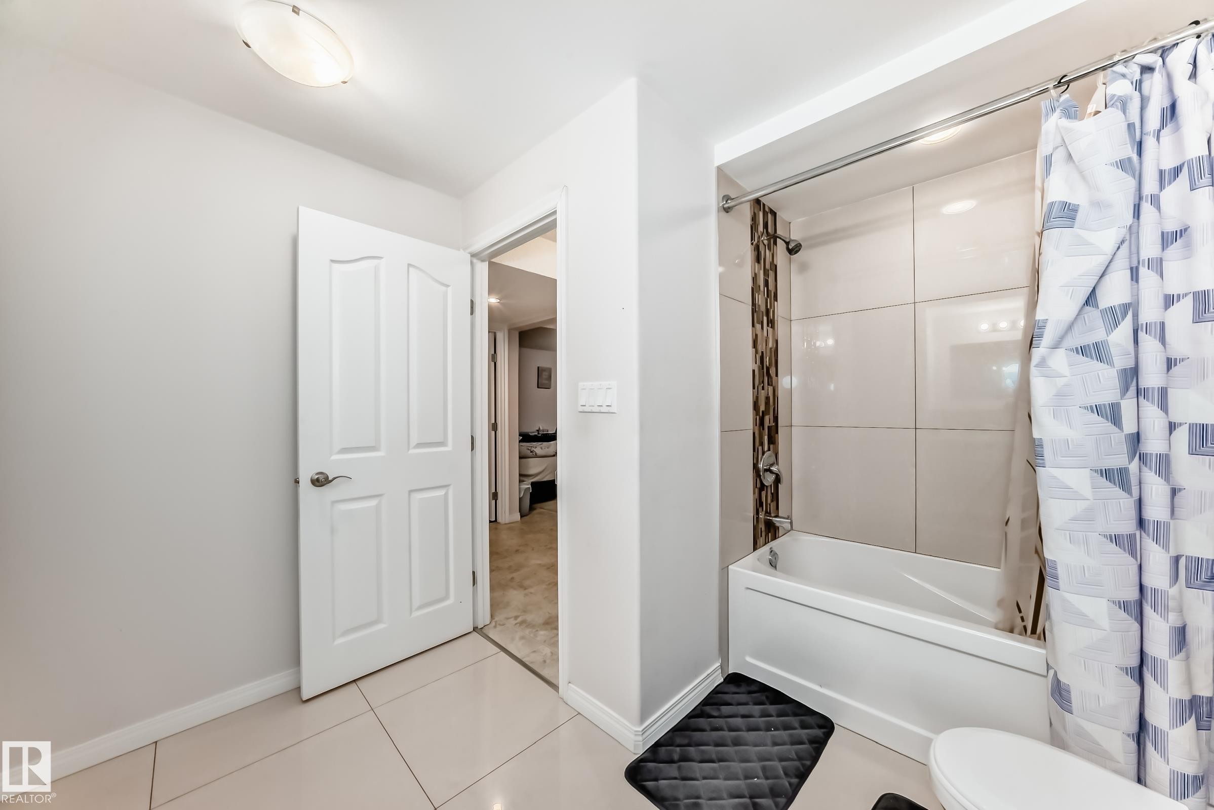 The bathroom features a white bathtub with a tiled shower surround, light-colored floor tiles, and a white door with a brushed nickel handle - 19024 50 Avenue, Edmonton, AB - Indoor Photo Showing Bathroom