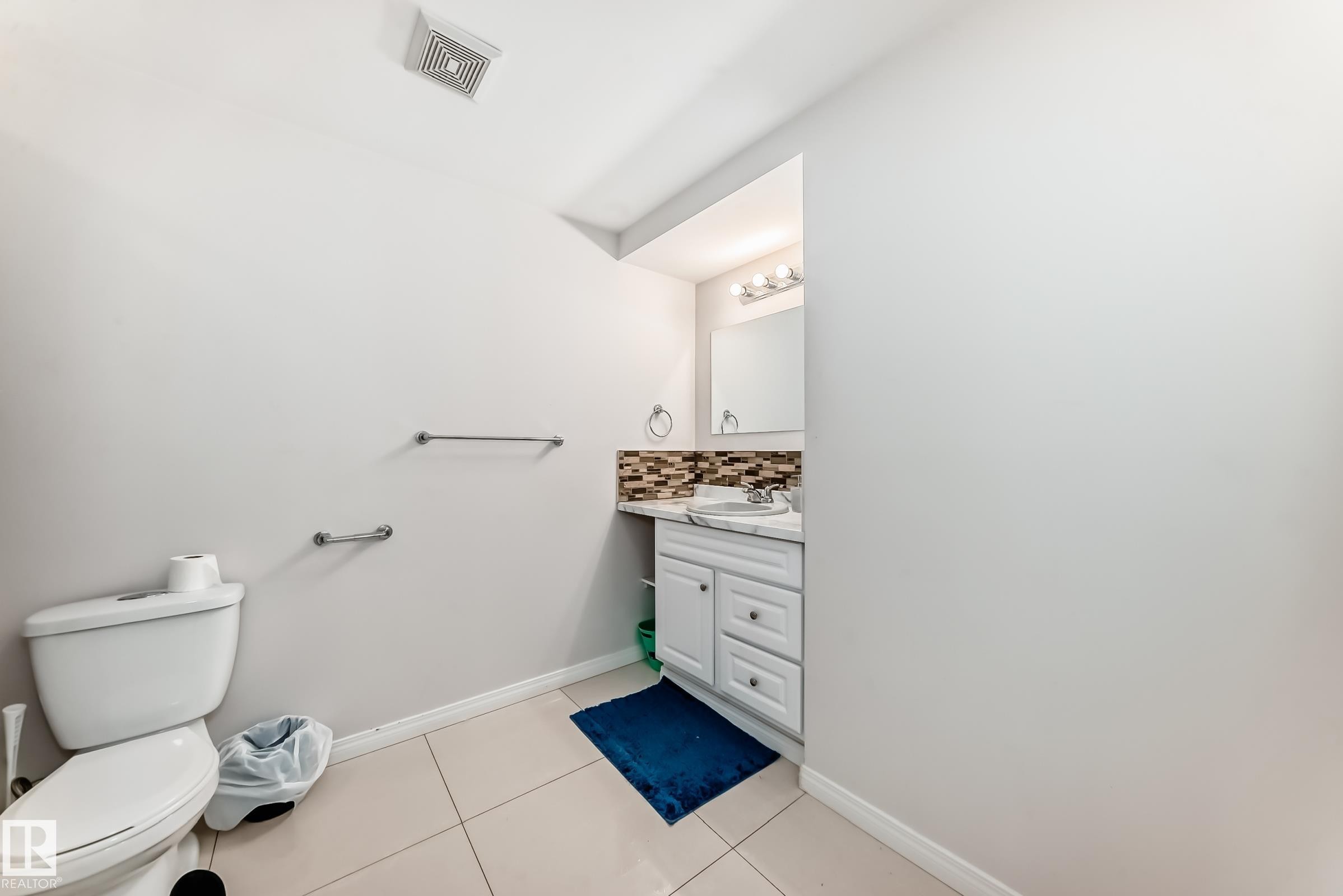 The bathroom features a white vanity with a rectangular sink, a decorative tiled backsplash, and a wall-mounted mirror with overhead lighting - 19024 50 Avenue, Edmonton, AB - Indoor Photo Showing Bathroom