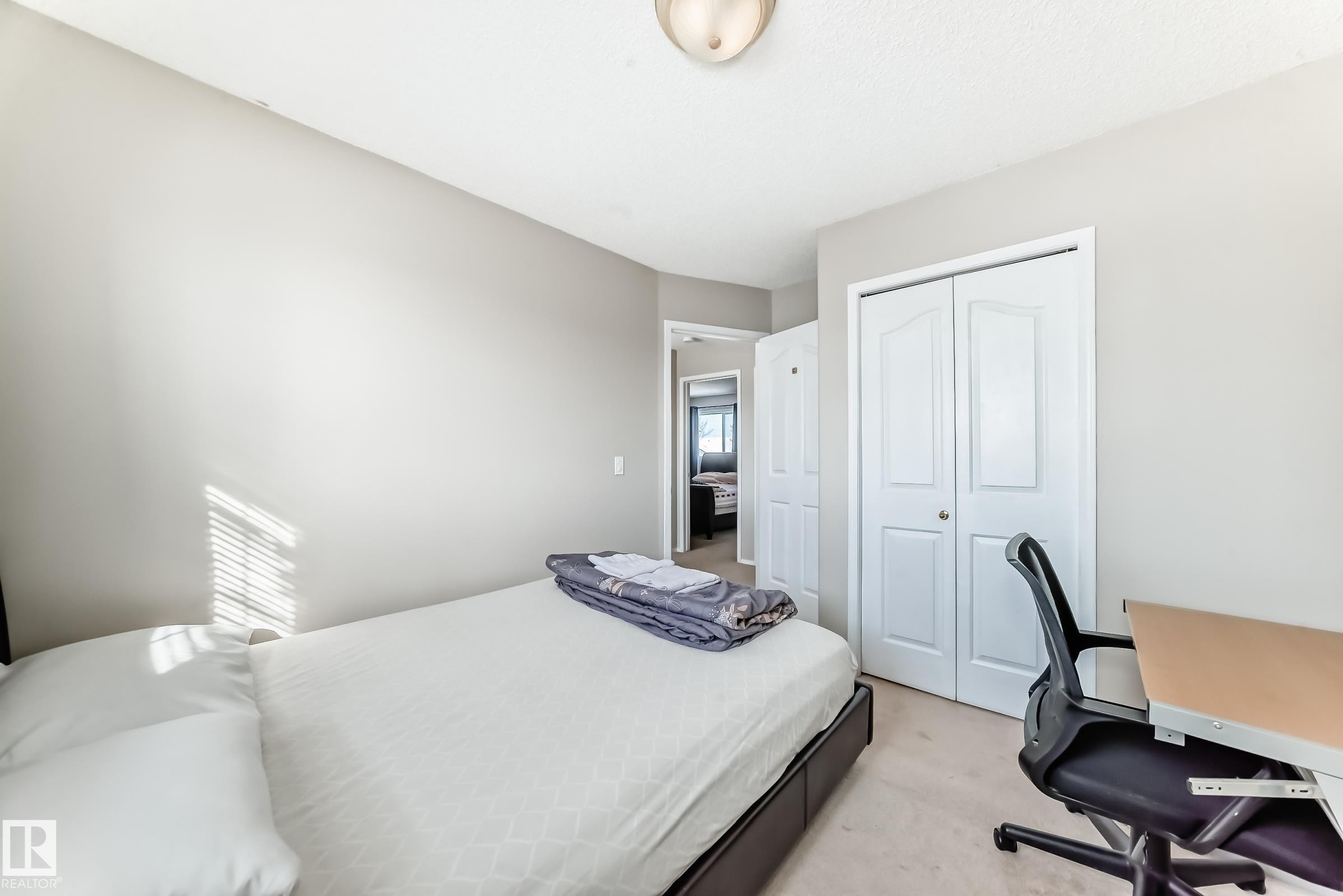The room features a neutral color palette, a bed with a dark bed frame, and a closet with white bi-fold doors - 19024 50 Avenue, Edmonton, AB - Indoor Photo Showing Bedroom