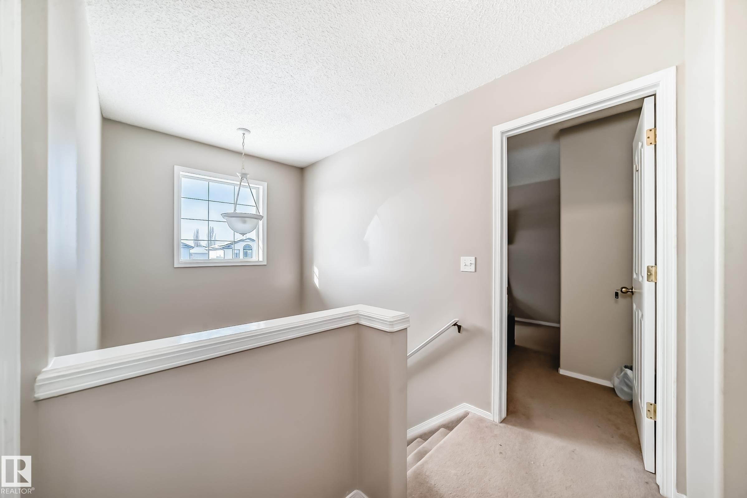 This landing features neutral-toned walls, a white window frame, and a hanging light fixture - 19024 50 Avenue, Edmonton, AB - Indoor Photo Showing Other Room