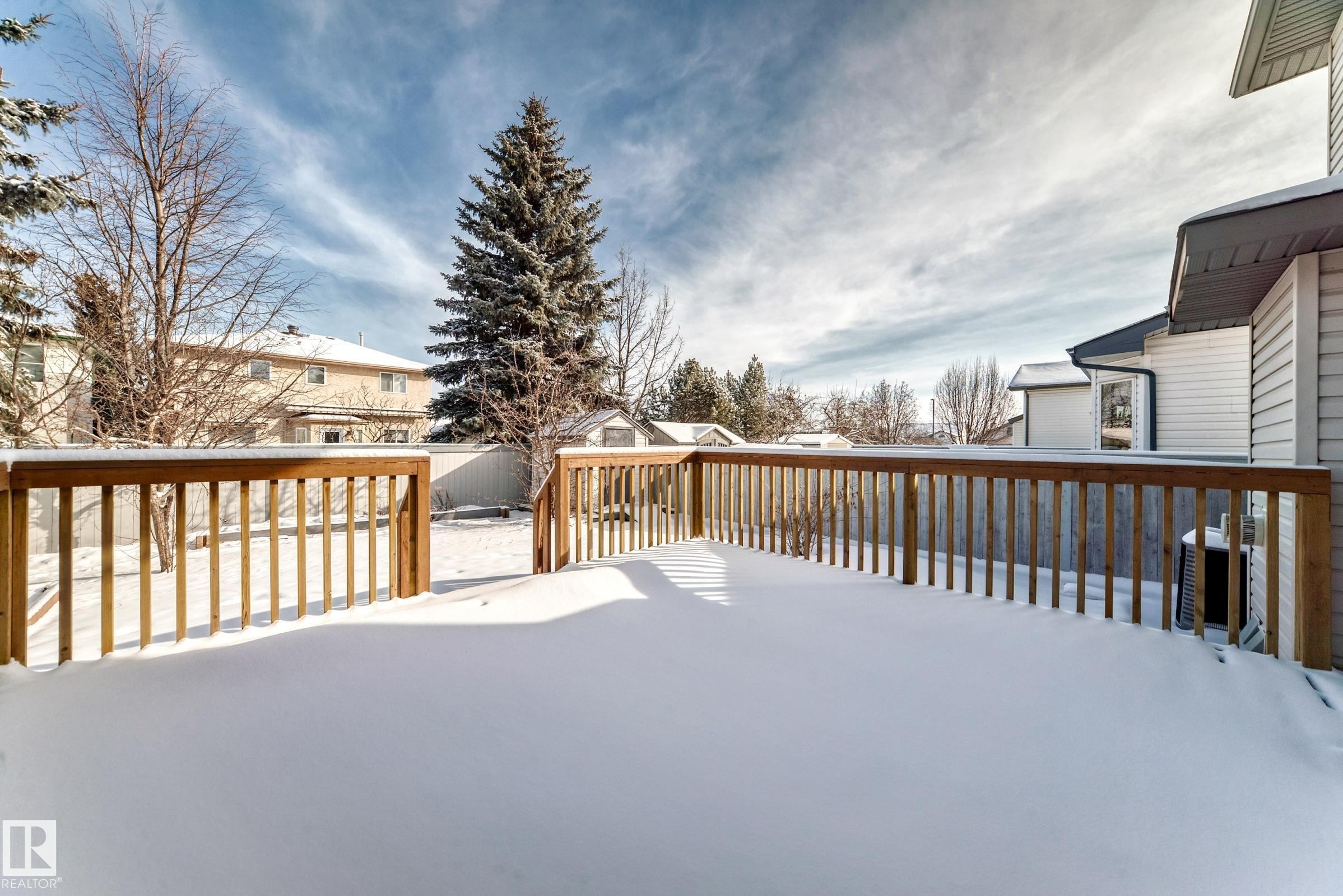 The property features an extensive deck with wooden railings, overlooking a yard with mature trees - 19024 50 Avenue, Edmonton, AB - Outdoor With Exterior