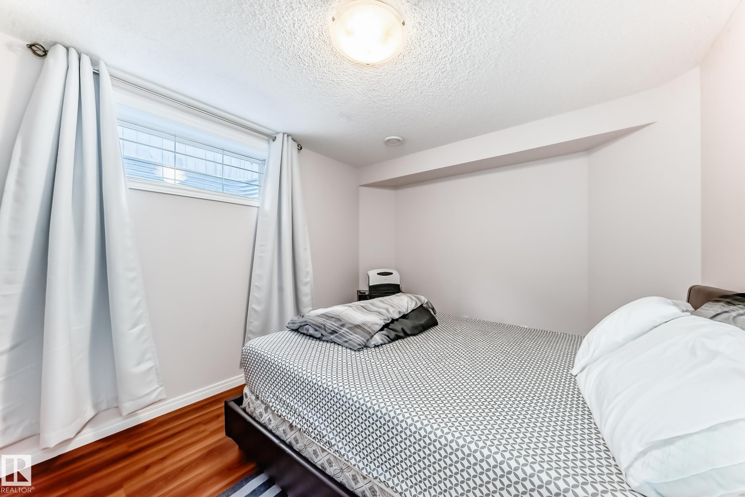 The property features light hardwood floors, light-colored walls, and a window with white blinds and light curtains - 19024 50 Avenue, Edmonton, AB - Indoor Photo Showing Bedroom