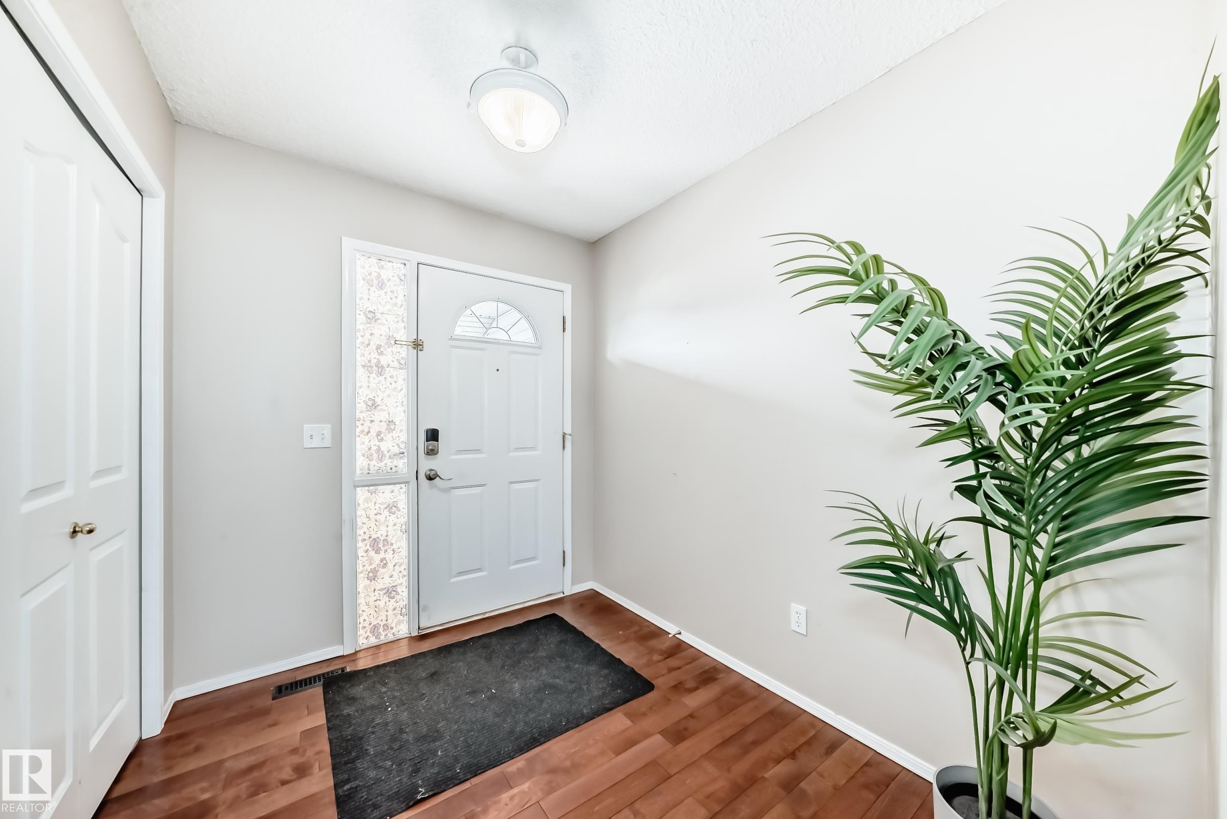 Inviting entryway featuring warm-toned wood flooring, a white paneled door with decorative glass, and a functional closet - 19024 50 Avenue, Edmonton, AB - Indoor Photo Showing Other Room