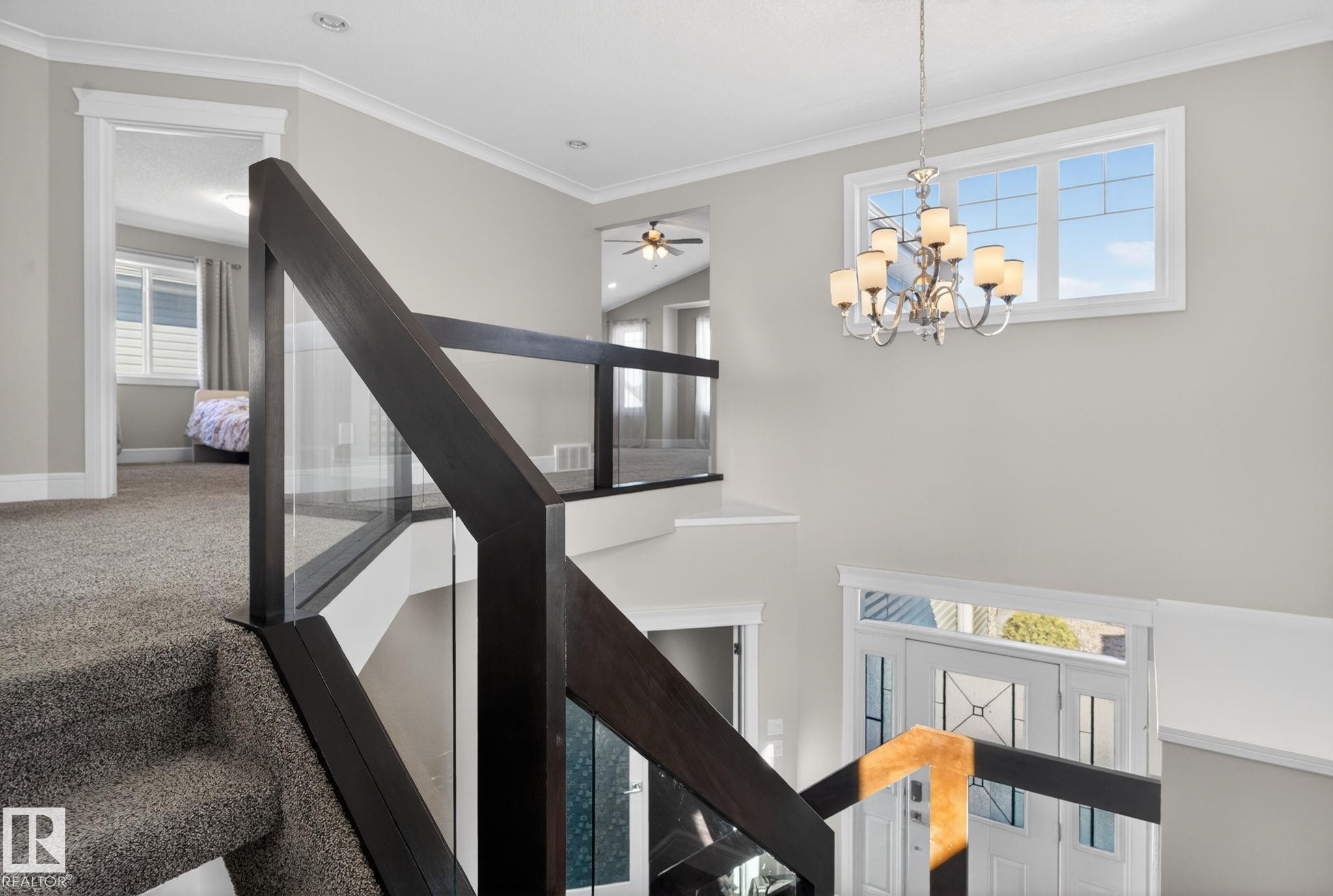 A welcoming entry area featuring a contemporary chandelier and a glass panel staircase with dark wood railings - 4134 Charles Link, Edmonton, AB - Indoor Photo Showing Other Room