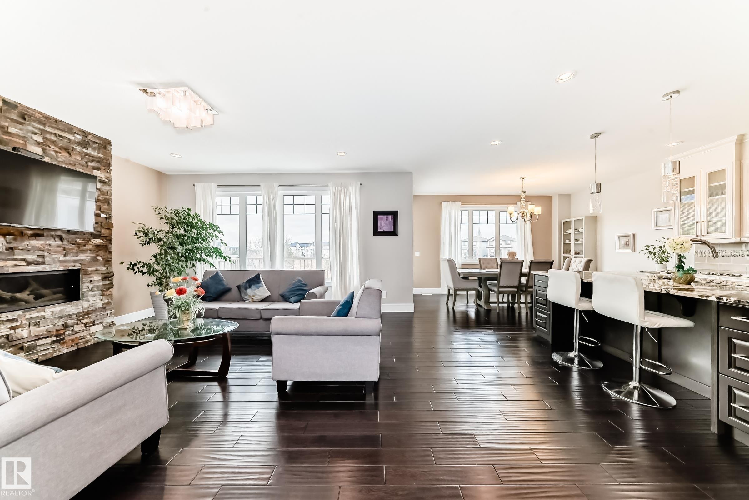 Open concept living area featuring dark hardwood floors, a stone-accented fireplace, and a dining area with a chandelier - 4134 Charles Link, Edmonton, AB - Indoor Photo Showing Living Room With Fireplace