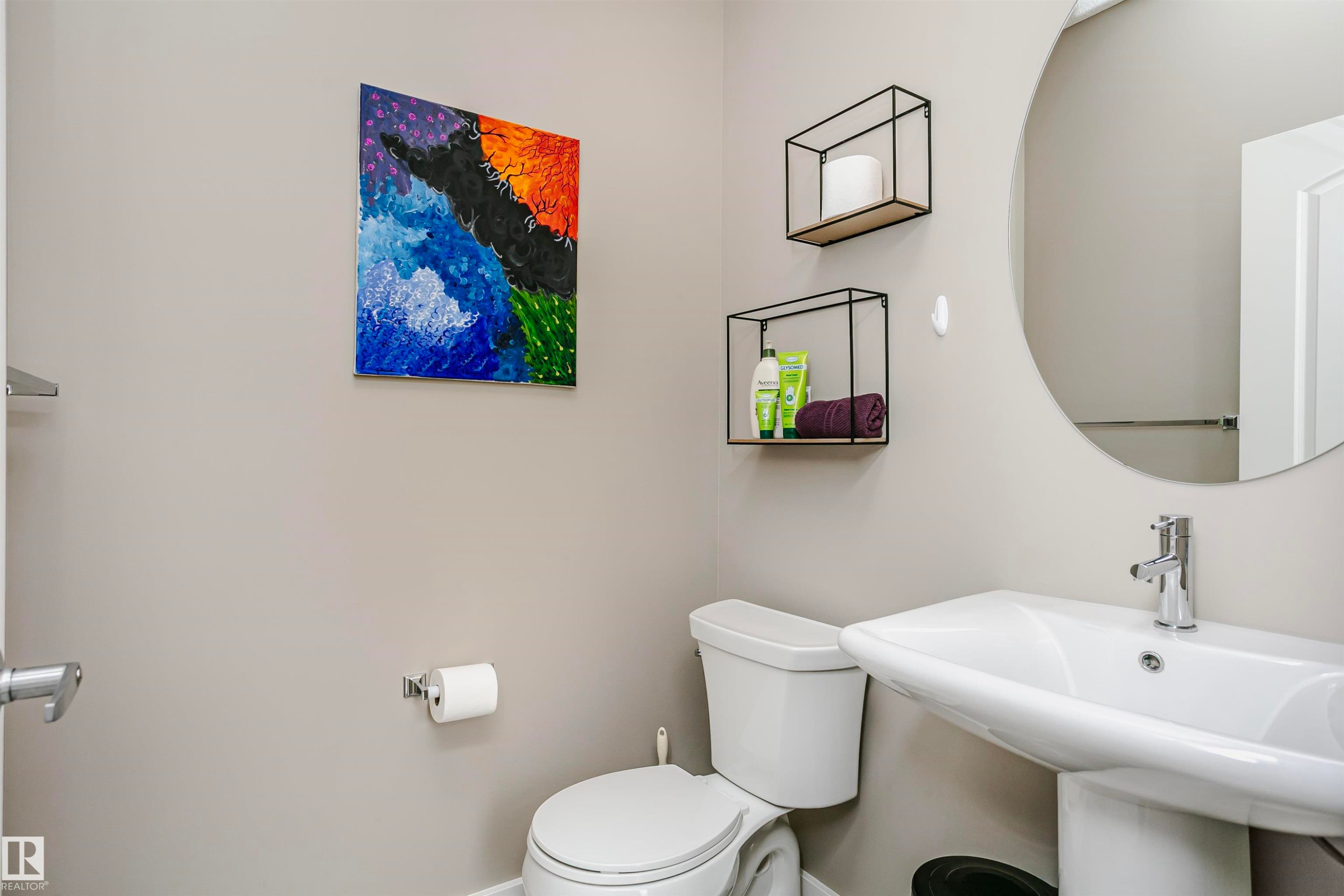The bathroom features a white pedestal sink, a circular mirror, and two wall-mounted open-frame shelves for storage - 6116 Rosenthal Way, Edmonton, AB - Indoor Photo Showing Bathroom