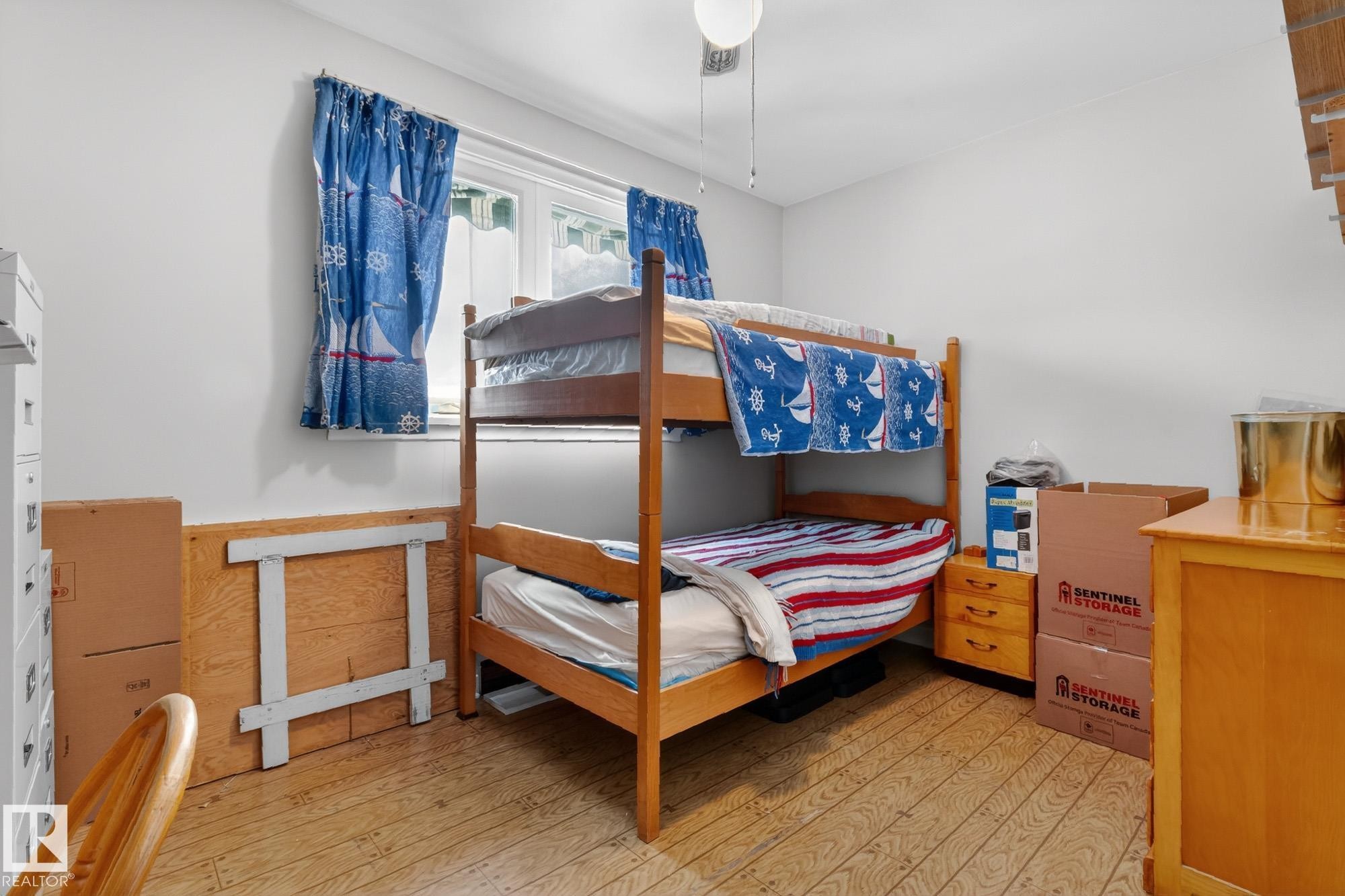 The room features light-colored flooring, a window with blue patterned curtains, and a ceiling fan - 11255 71 Avenue, Edmonton, AB - Indoor Photo Showing Bedroom