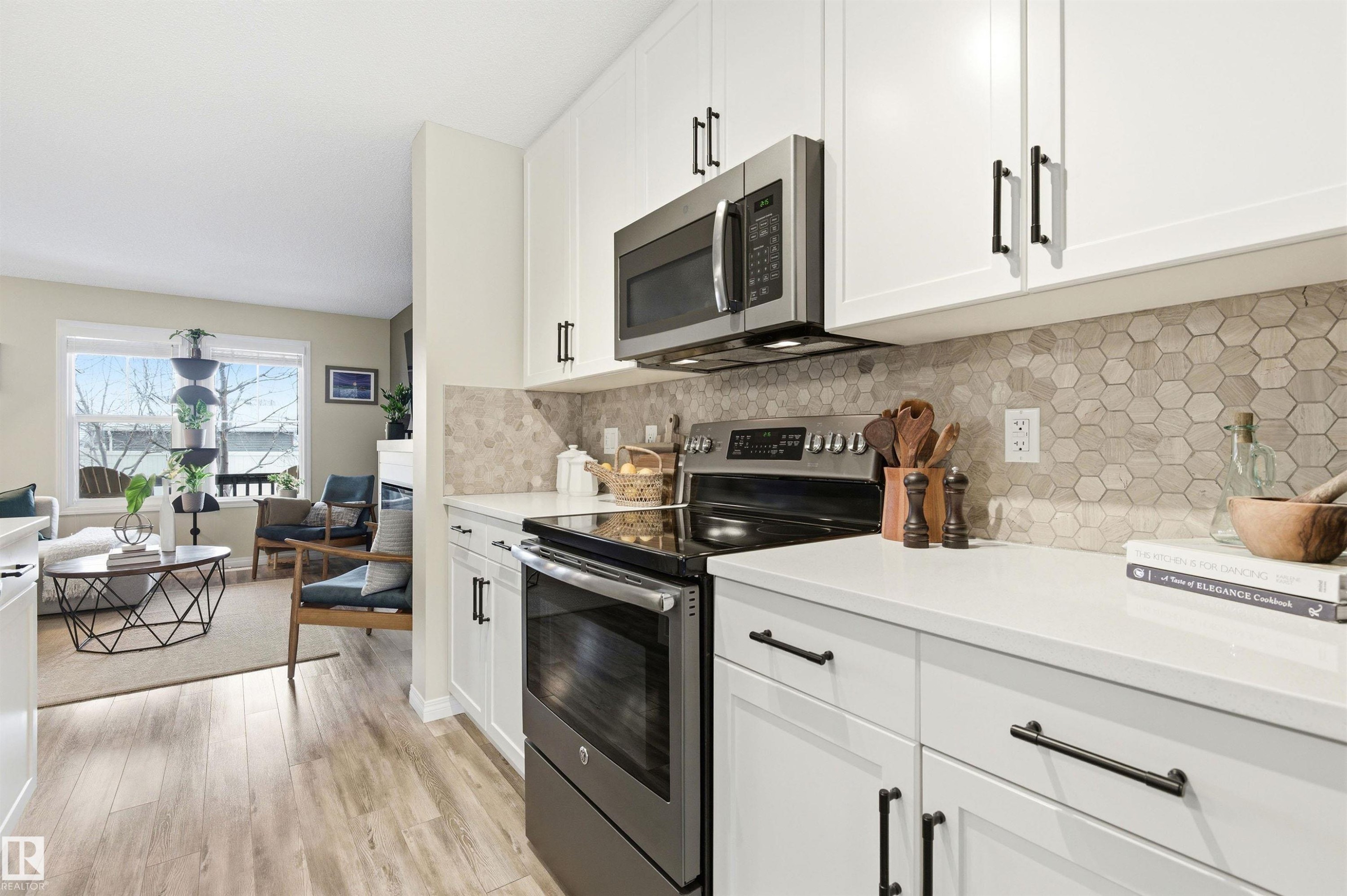 The kitchen features white cabinetry with black hardware, stainless steel appliances, and a hexagon tile backsplash - 3247 Cherry Crescent, Edmonton, AB - Indoor Photo Showing Kitchen With Upgraded Kitchen