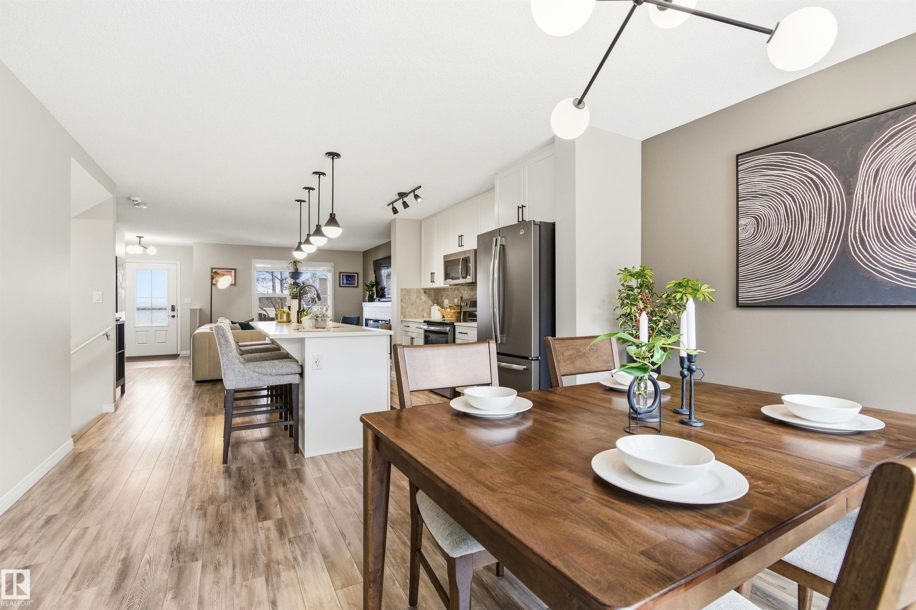 Open-concept living area featuring light-toned flooring, a kitchen island with pendant lighting, and a dining area with a modern chandelier - 3247 Cherry Crescent, Edmonton, AB - Indoor