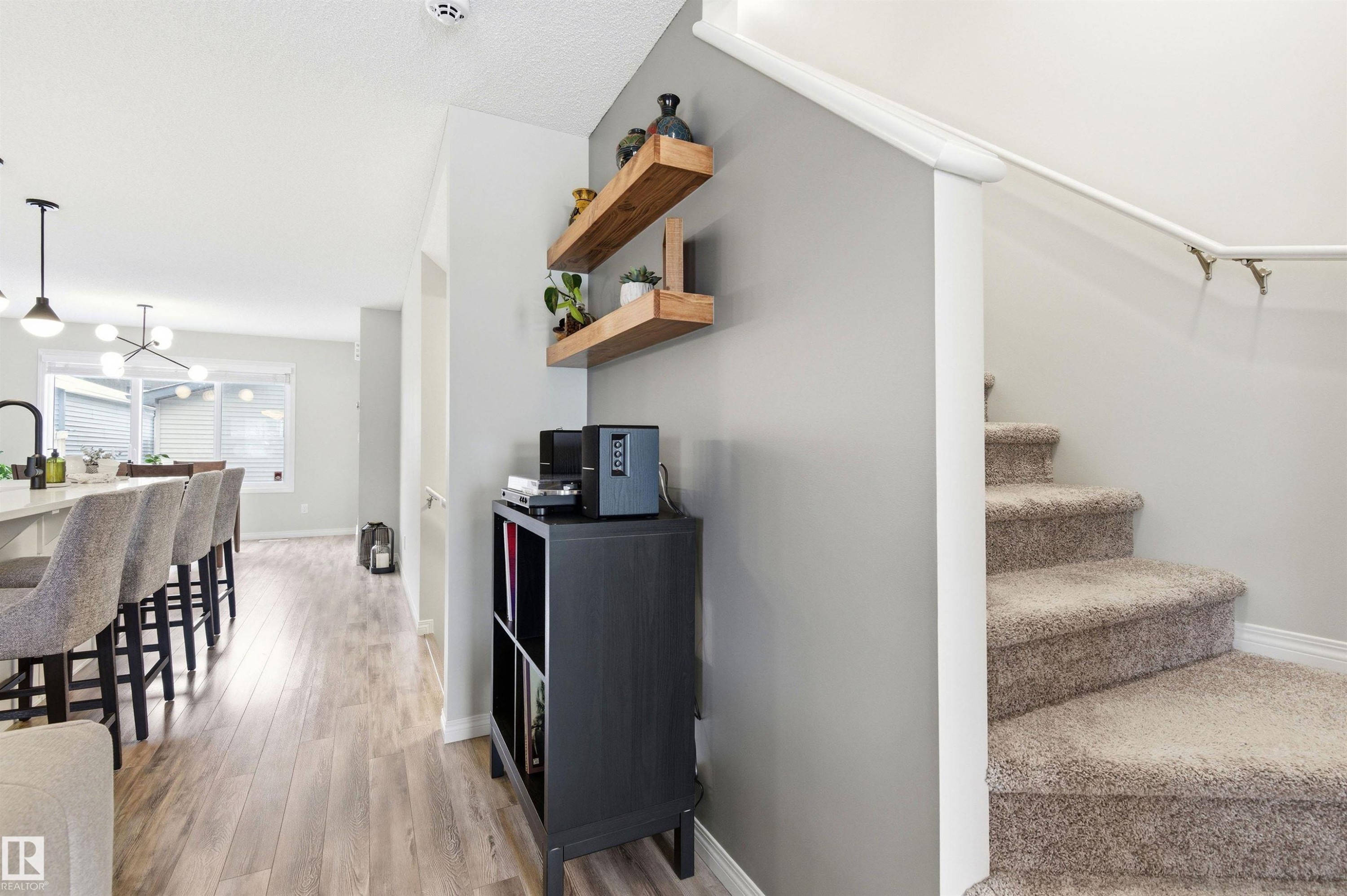 Interior featuring light wood-style flooring, a staircase with carpeted treads, and built-in wooden shelves on a grey wall - 3247 Cherry Crescent, Edmonton, AB - Indoor