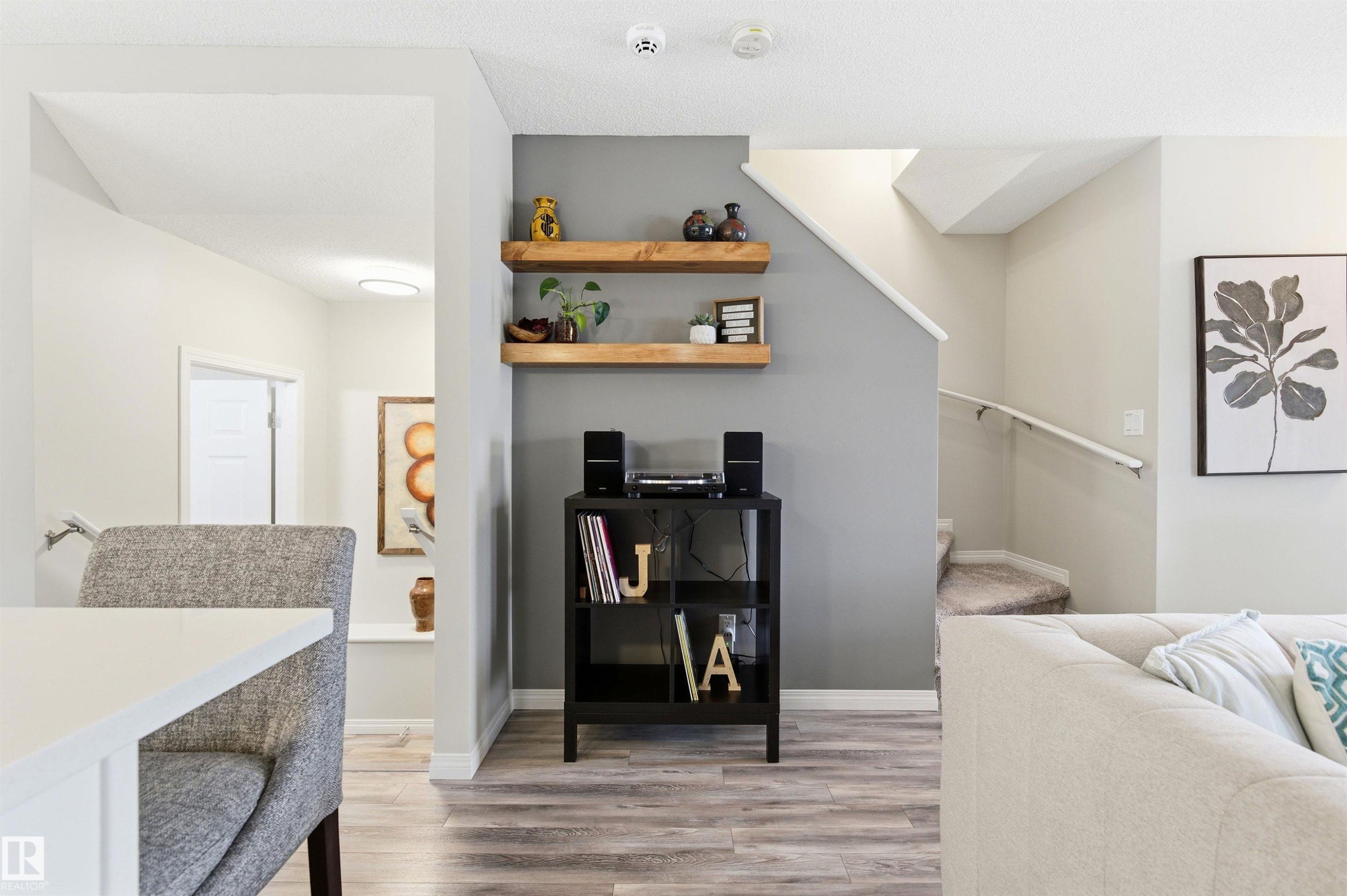 This inviting interior space features light wood-style flooring, a staircase with a handrail and carpeted steps, and warm neutral wall colors - 3247 Cherry Crescent, Edmonton, AB - Indoor Photo Showing Other Room
