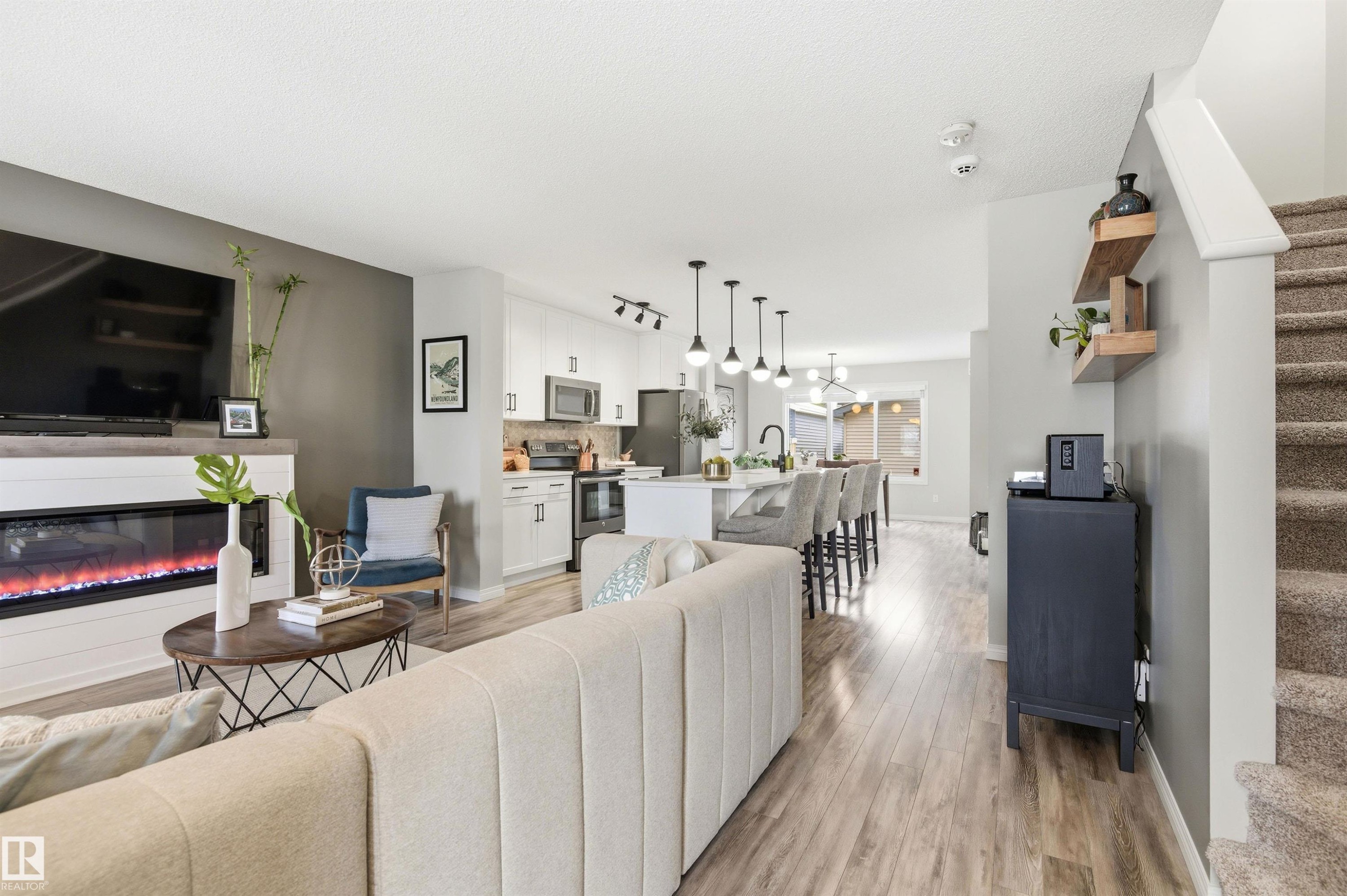 Living area featuring wood-style flooring, an electric fireplace with a white shiplap-style surround, and an open layout to the kitchen - 3247 Cherry Crescent, Edmonton, AB - Indoor Photo Showing Living Room With Fireplace