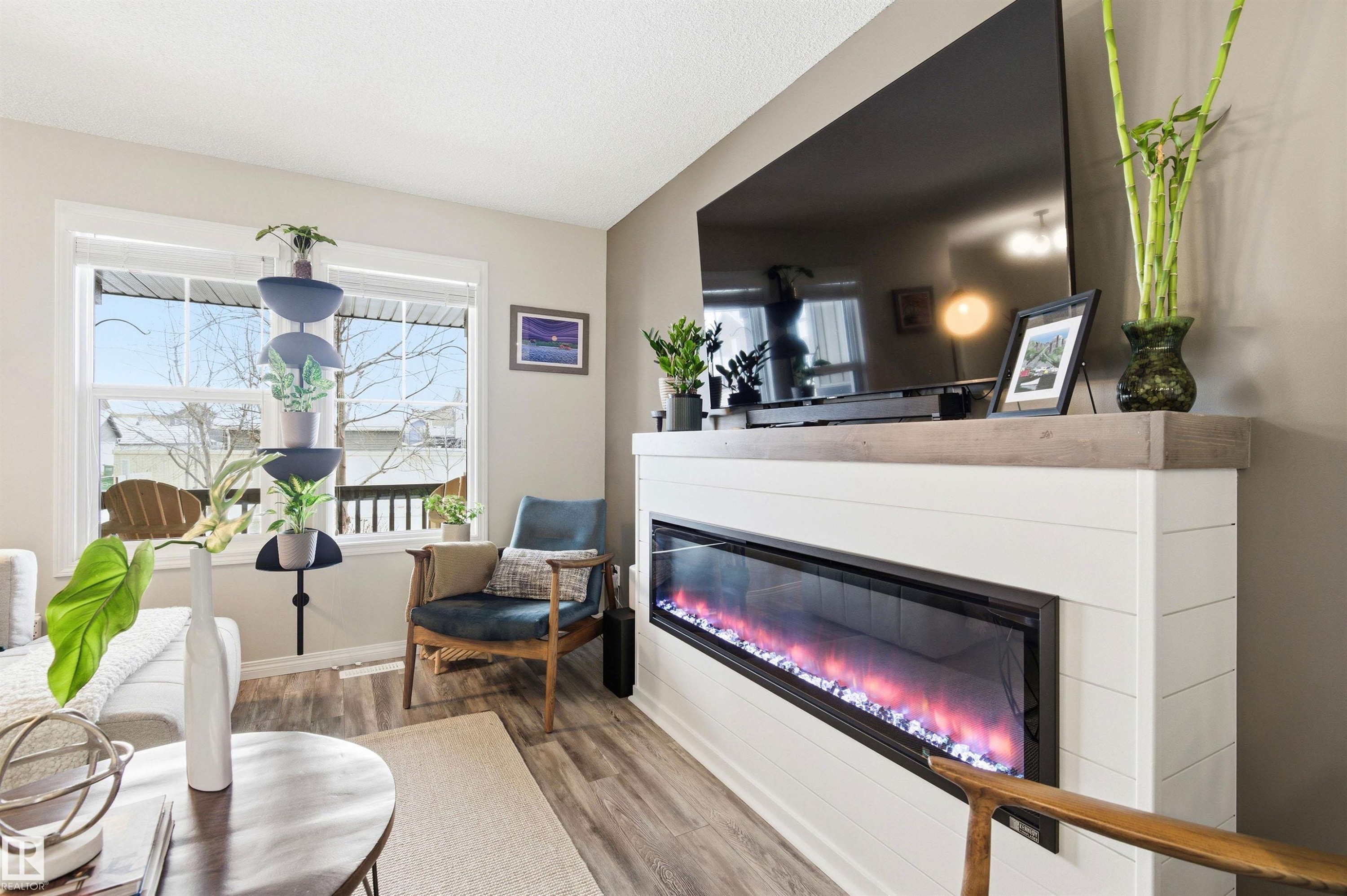 The living area features wood-style flooring, a large window, and a fireplace with a white shiplap-style facade and a light wood-tone mantel - 3247 Cherry Crescent, Edmonton, AB - Indoor Photo Showing Living Room With Fireplace