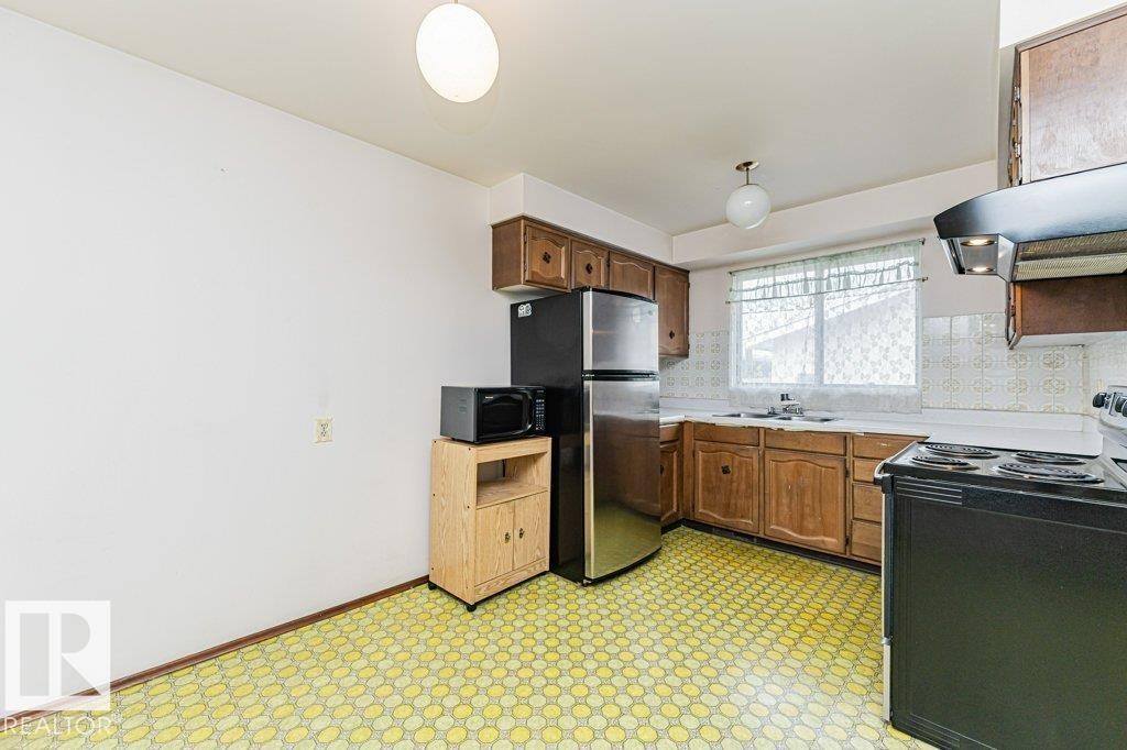 The kitchen features wood cabinetry, a window with a sheer curtain, and a patterned floor - 8804 19 Avenue, Edmonton, AB - Indoor Photo Showing Kitchen