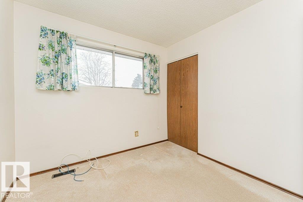This room features light-colored carpeting, white walls, and a window with floral curtains - 8804 19 Avenue, Edmonton, AB - Indoor Photo Showing Other Room