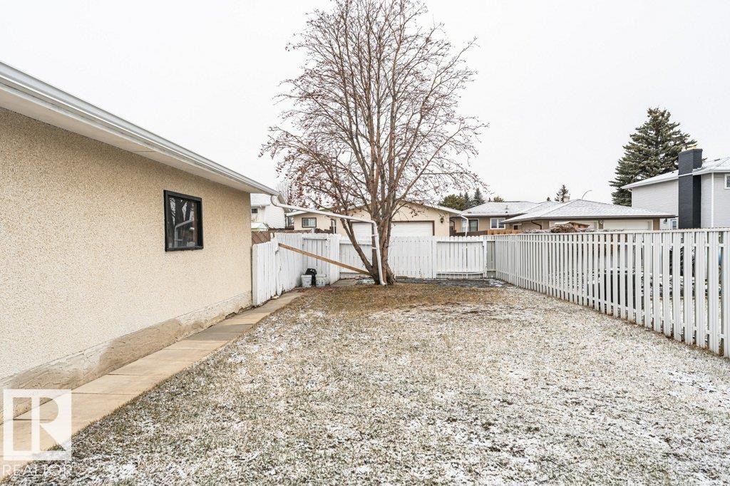 The property includes a spacious backyard with a white picket fence, a mature tree, and a paved pathway leading to the rear of the home - 8804 19 Avenue, Edmonton, AB - Outdoor