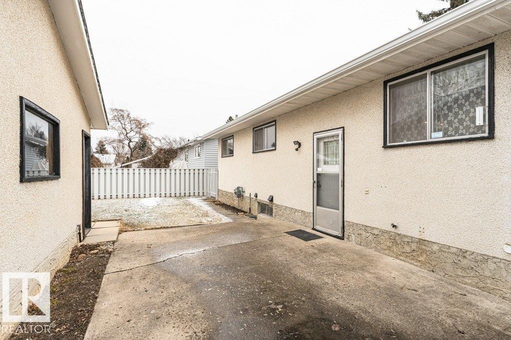 The property features a concrete paved area leading to an exterior door, with a white picket fence visible in the background - 8804 19 Avenue, Edmonton, AB - Outdoor With Exterior
