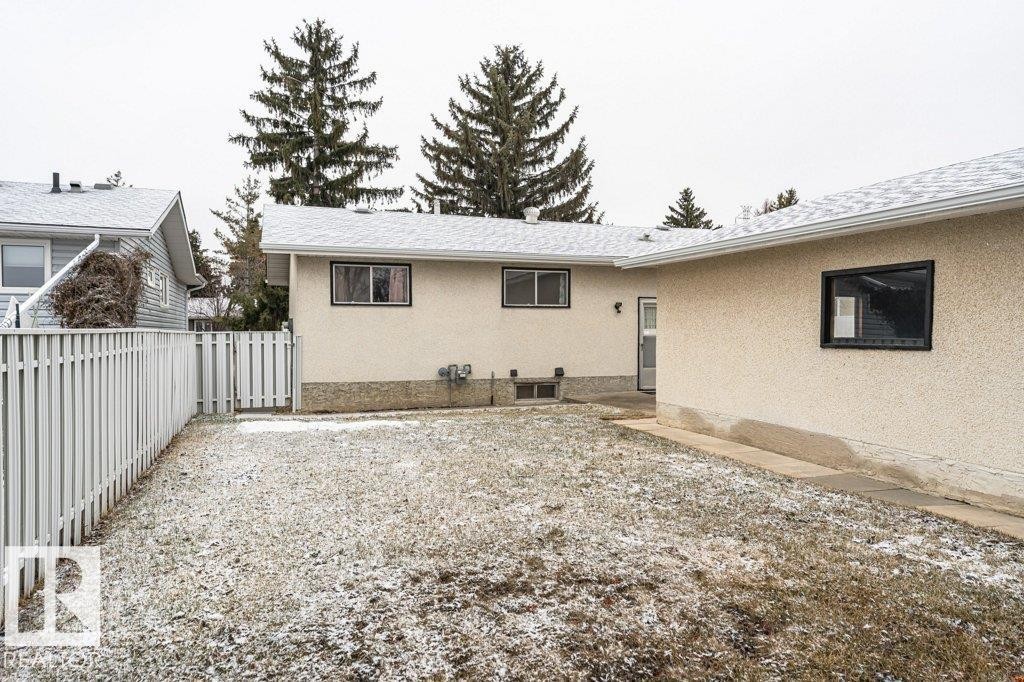 The property features an exterior with light-colored stucco and black-framed windows, complemented by a white picket fence - 8804 19 Avenue, Edmonton, AB - Outdoor
